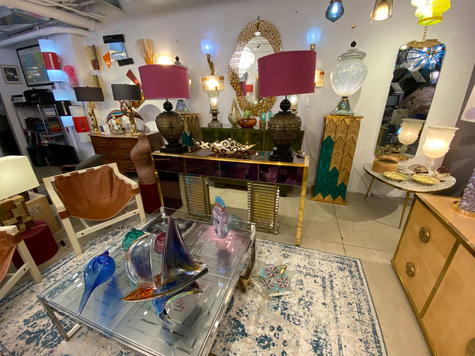 Colorful, eclectic furniture and decor display in a store, featuring lamps, vases, and decorative art pieces on tables and shelves.
