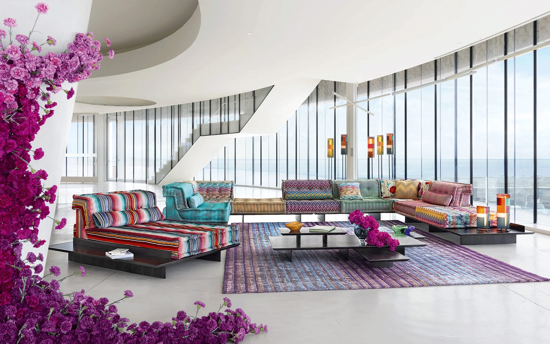 Modern living room with vibrant striped sofas, purple rug, and ocean view through floor-to-ceiling windows.