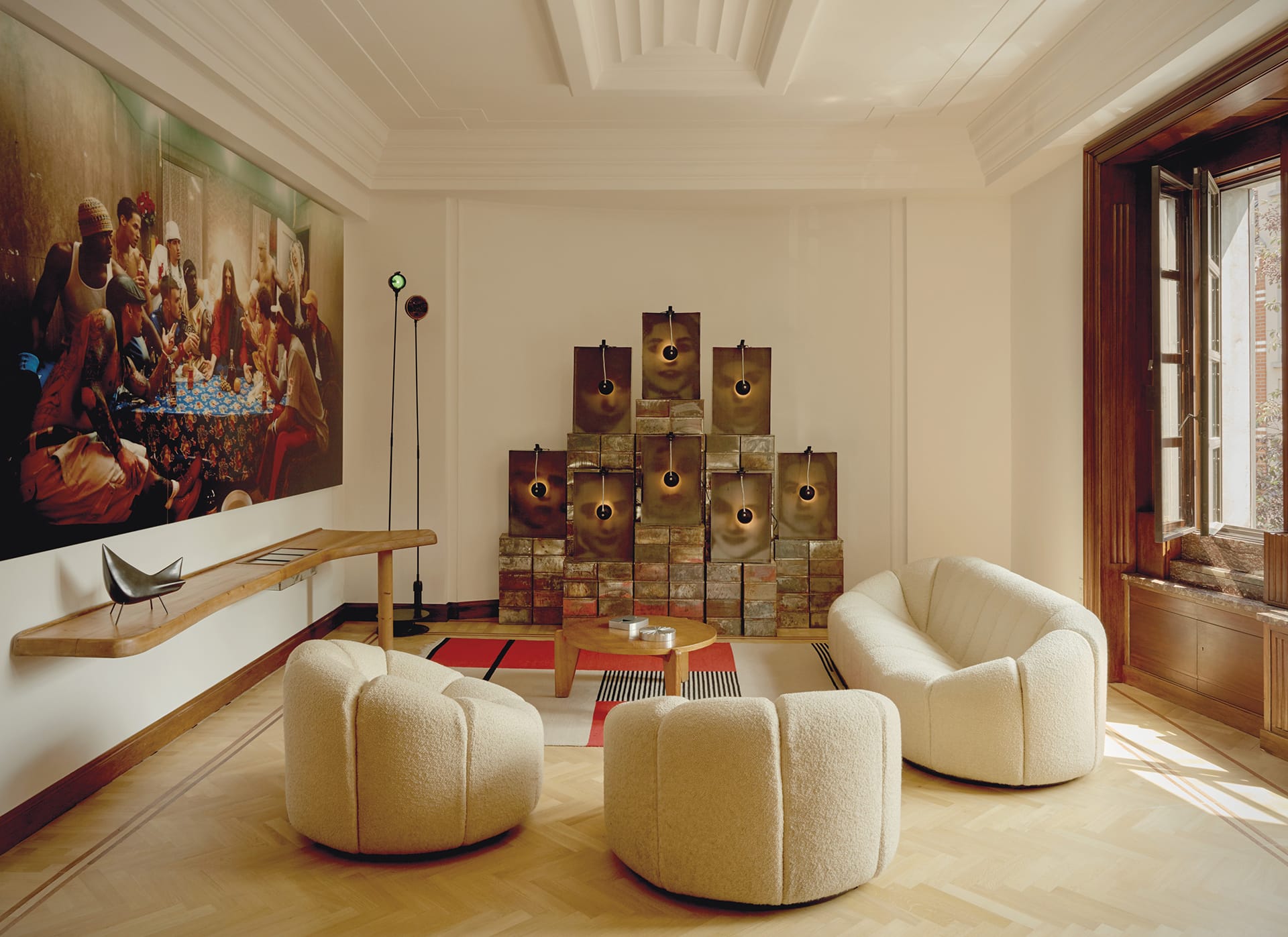 Modern living room with cream armchairs, a wooden table, and a wall art piece, featuring natural light through a large window.