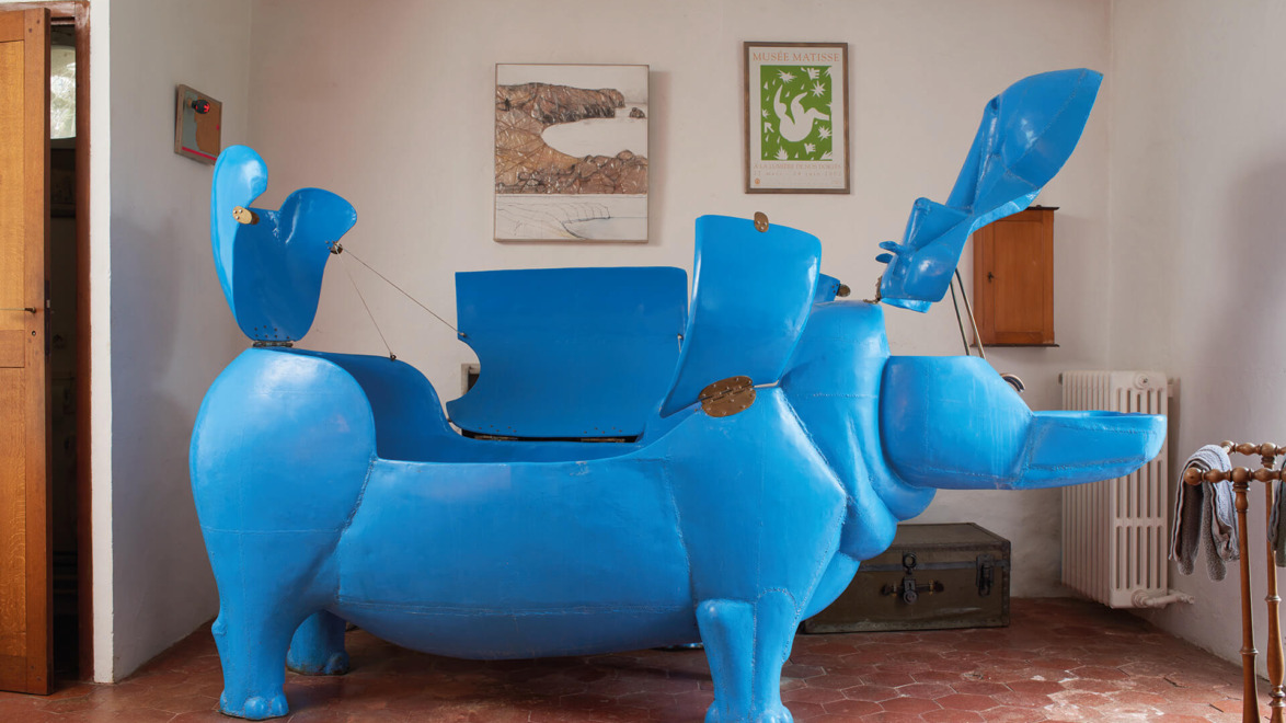 Blue hippopotamus-shaped chair sculpture with open compartments in an artfully decorated room.