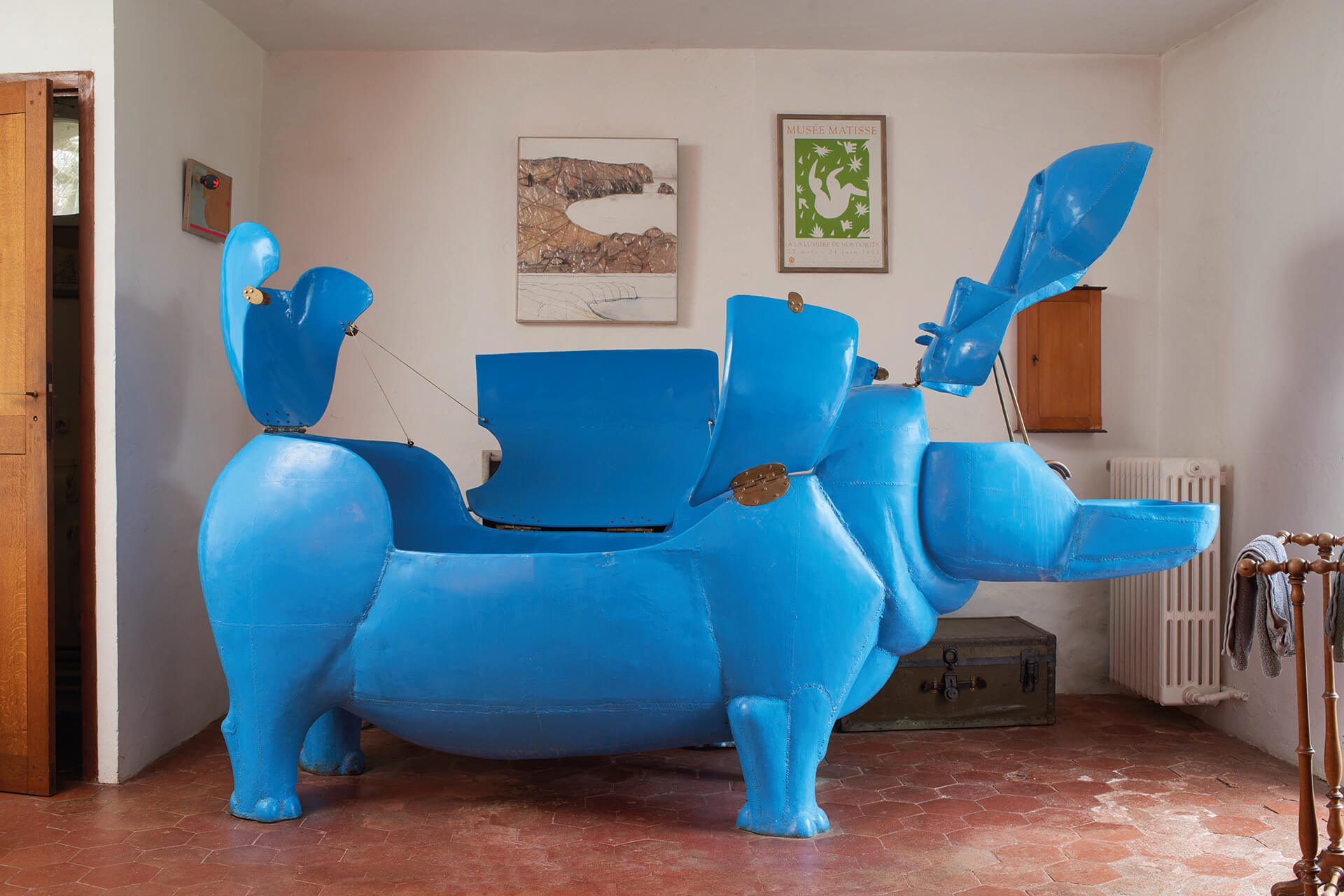 Blue hippopotamus-shaped chair sculpture with open compartments in an artfully decorated room.