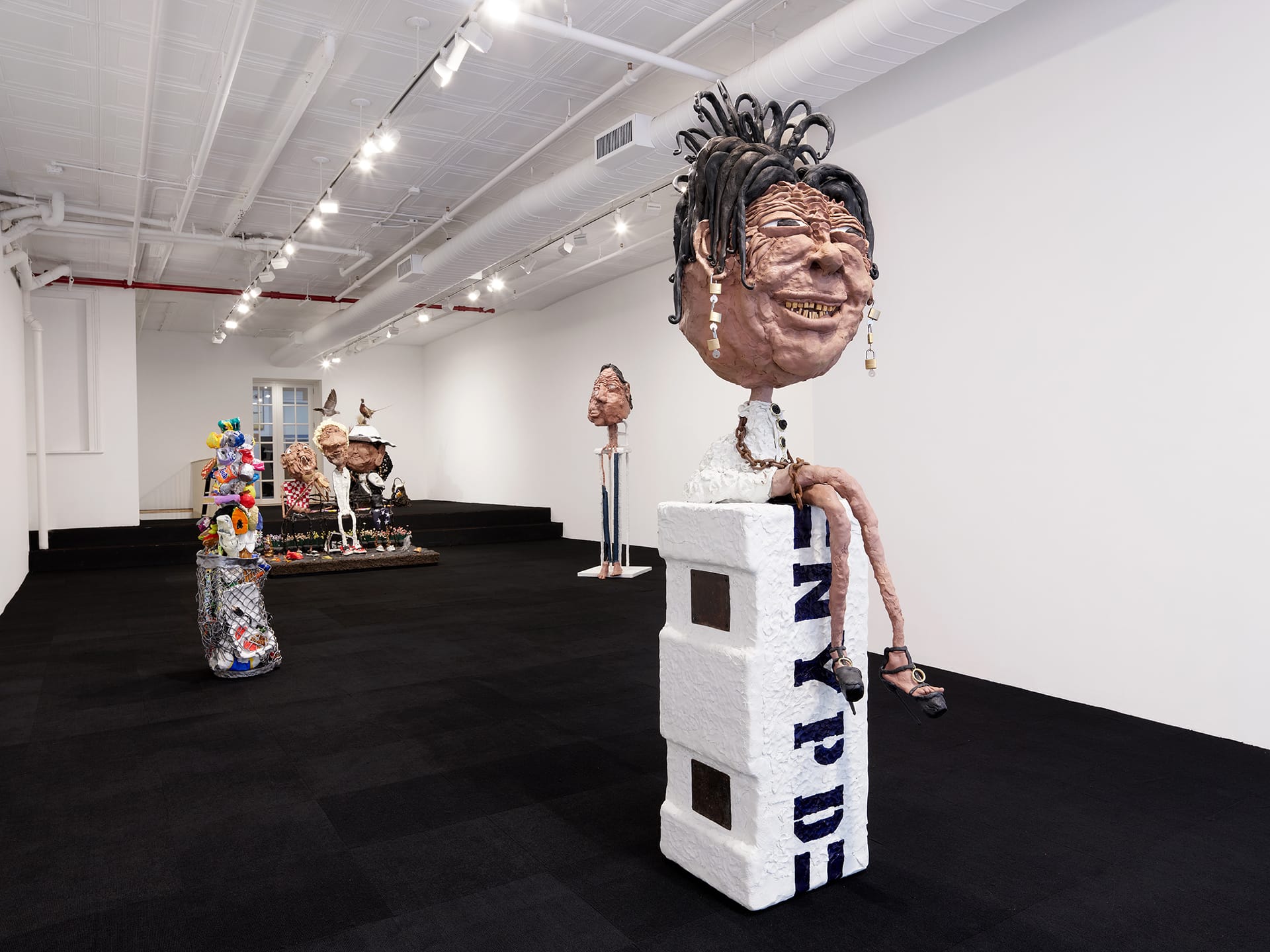 Art gallery with various abstract sculptures, including a large figure with a distinctive head seated on a white block.