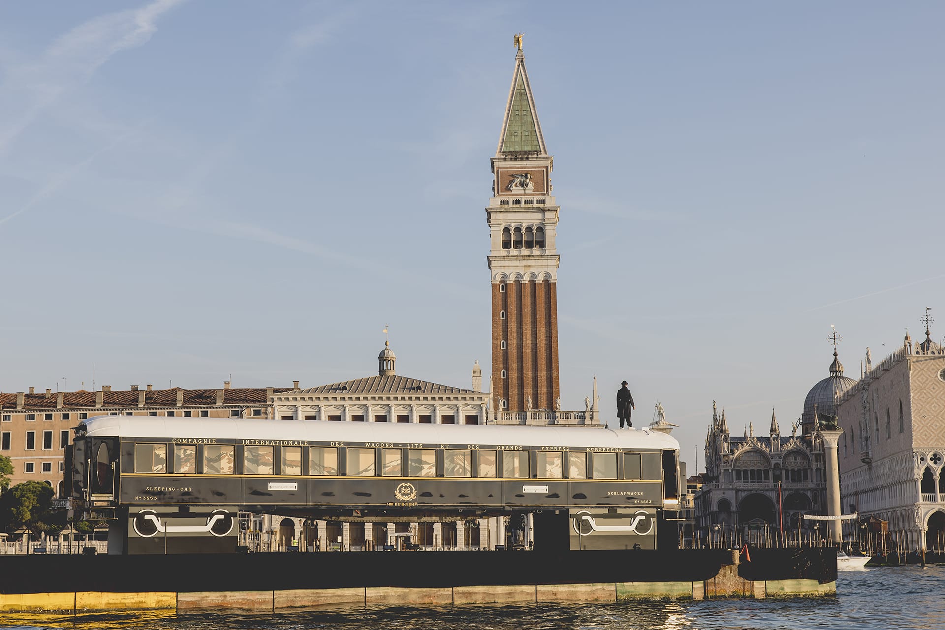 Train on water with St. Mark's Campanile in Venice in the background, part of unique artistic installation.