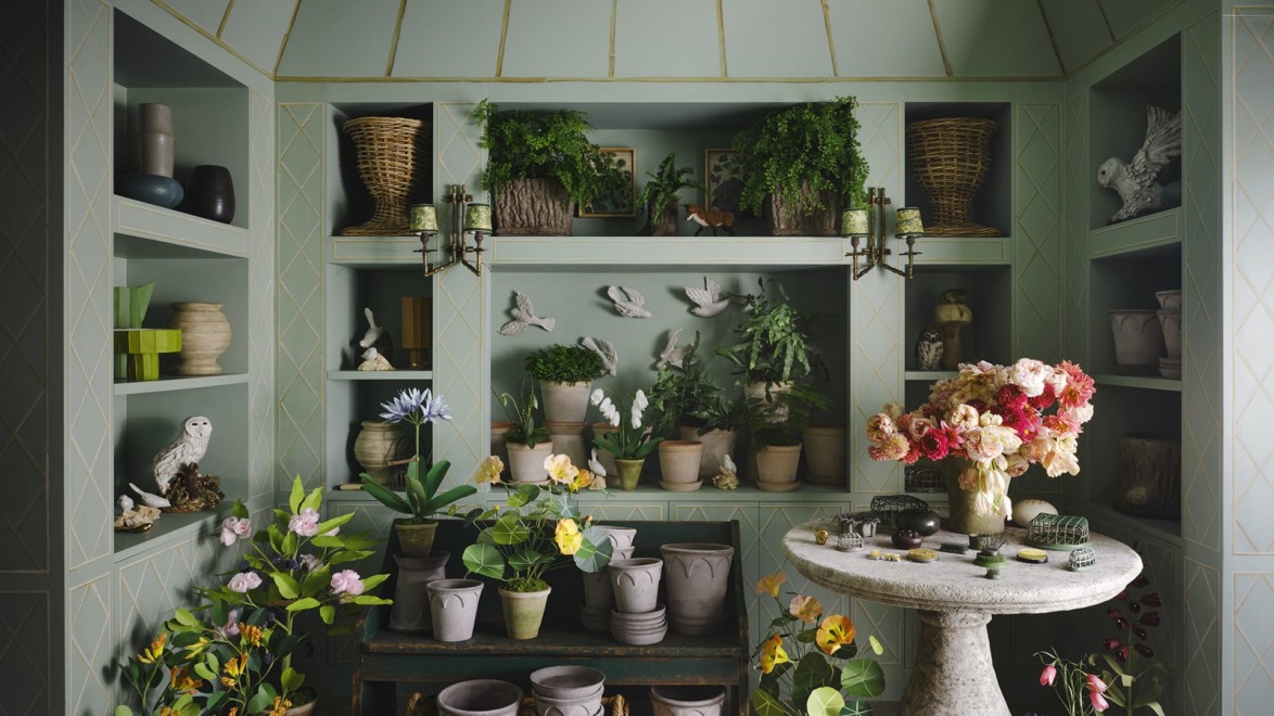 Indoor garden room with potted plants, flowers, and decorative elements on shelves and a round stone table.