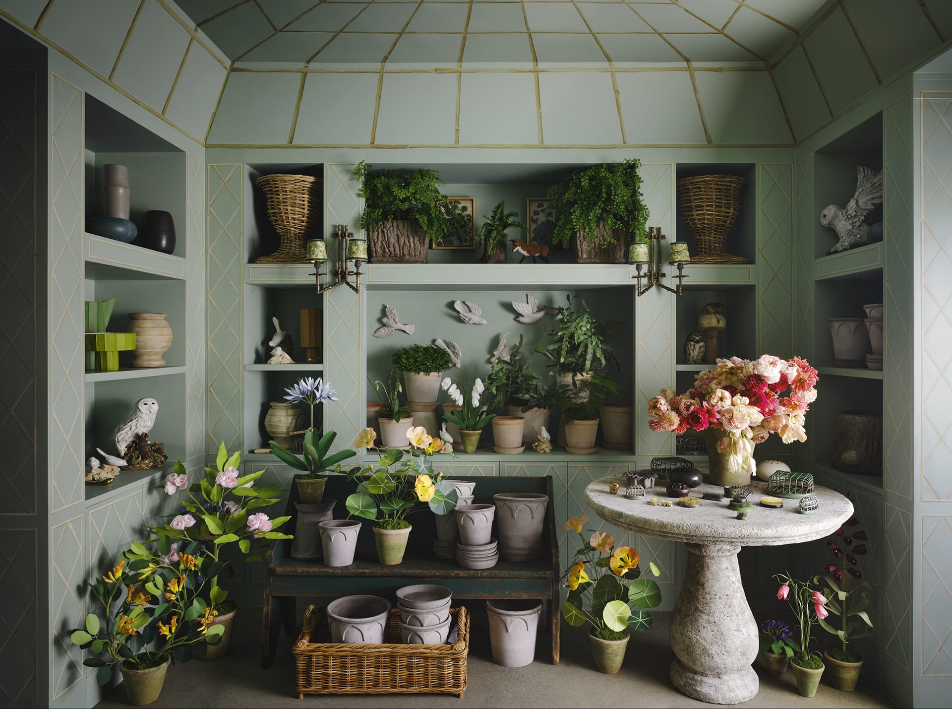 Indoor garden room with potted plants, flowers, and decorative elements on shelves and a round stone table.