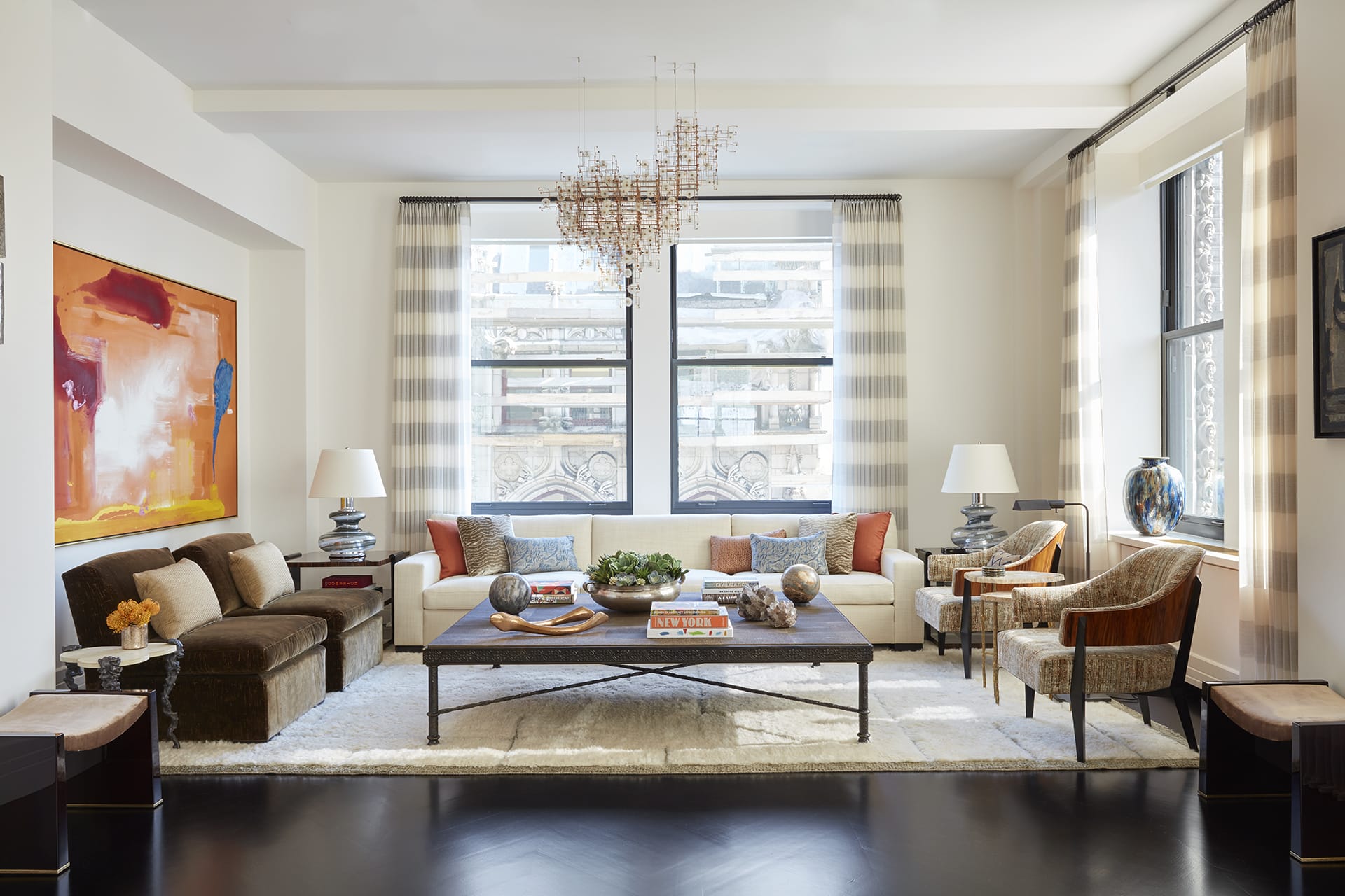 Modern living room with large windows, contemporary art, a chandelier, and elegant furniture in neutral tones.