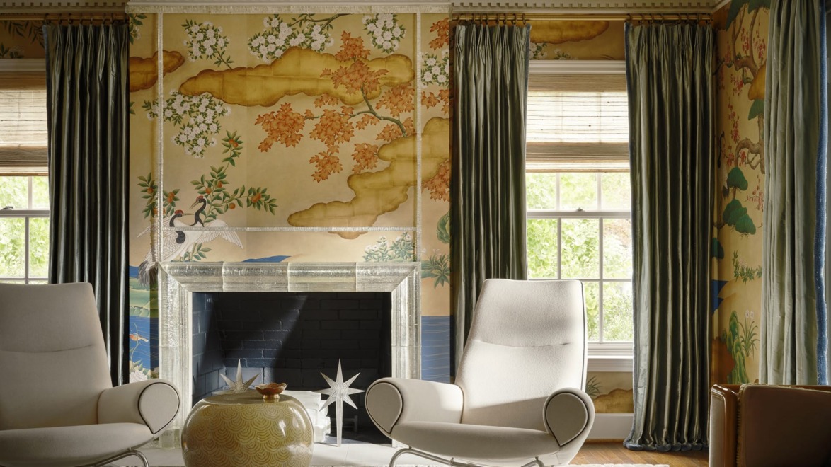Elegant living room with two modern chairs, an ornate fireplace, decorative wallpaper, and tall curtains.