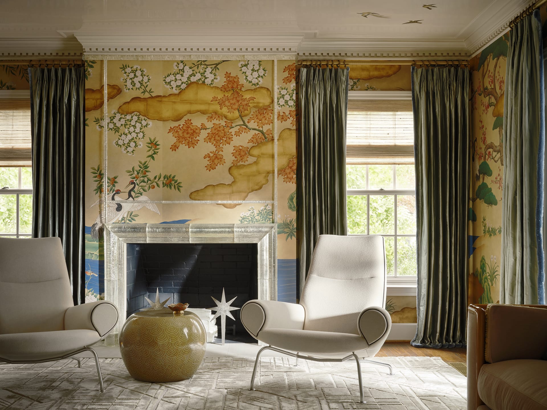 Elegant living room with two modern chairs, an ornate fireplace, decorative wallpaper, and tall curtains.
