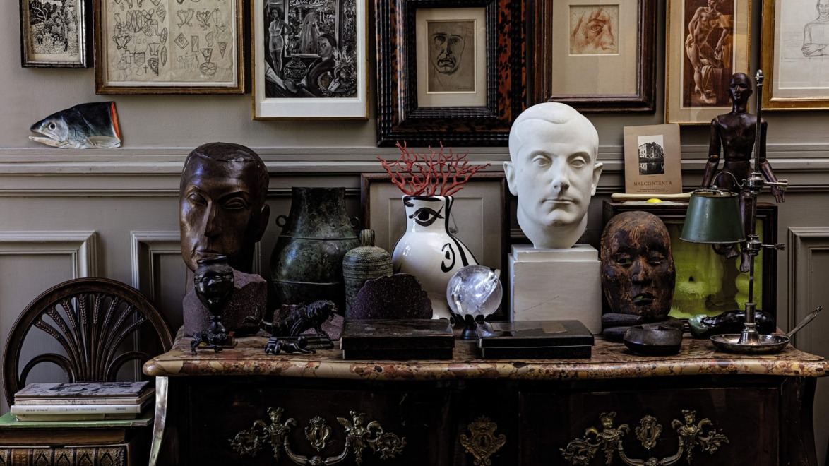 Eclectic art display with framed pictures, sculptures, and decorative items on a vintage dresser.