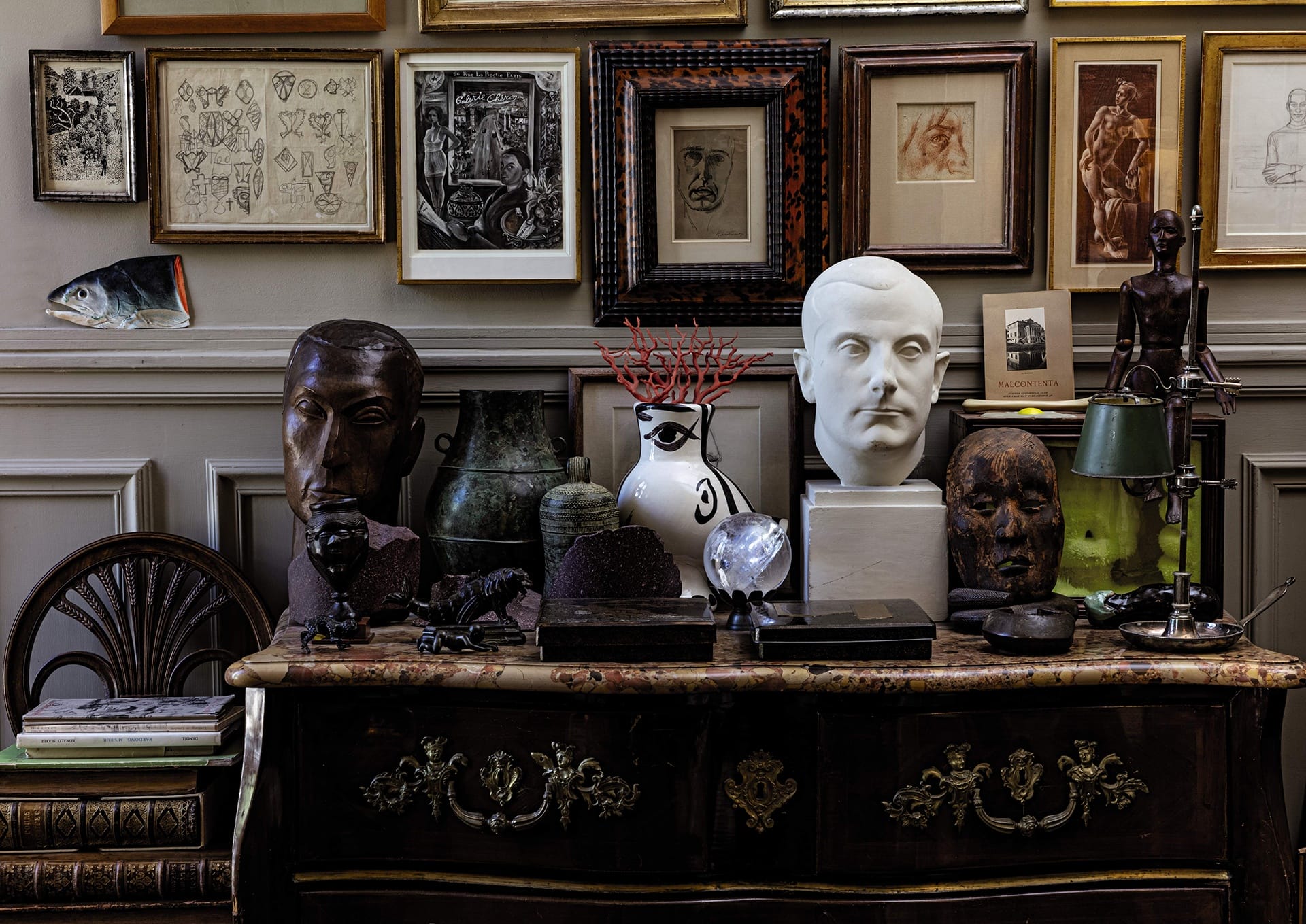 Eclectic art display with framed pictures, sculptures, and decorative items on a vintage dresser.