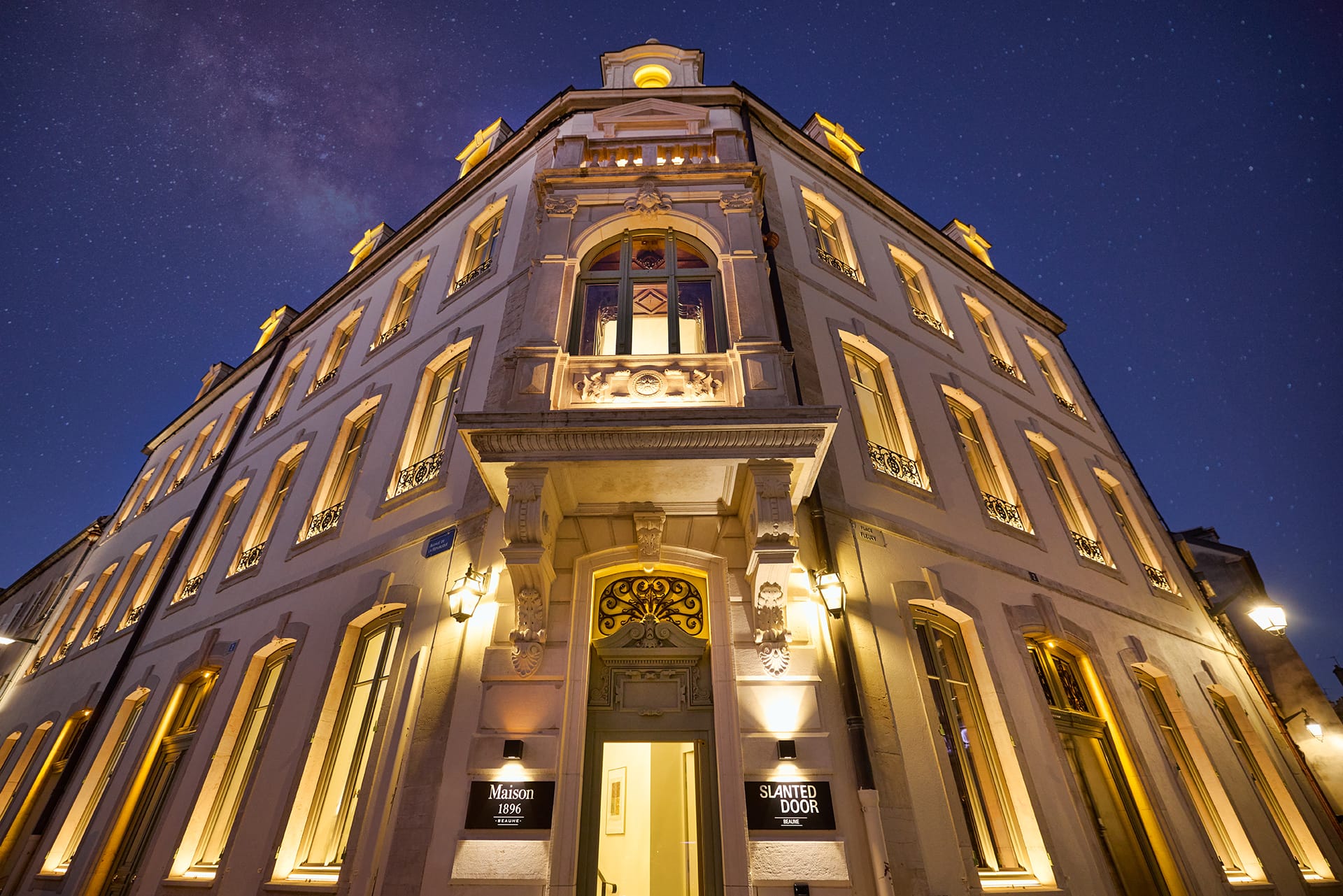 Exterior view of a well-lit historic building at night with decorative elements and a clear starry sky in the background