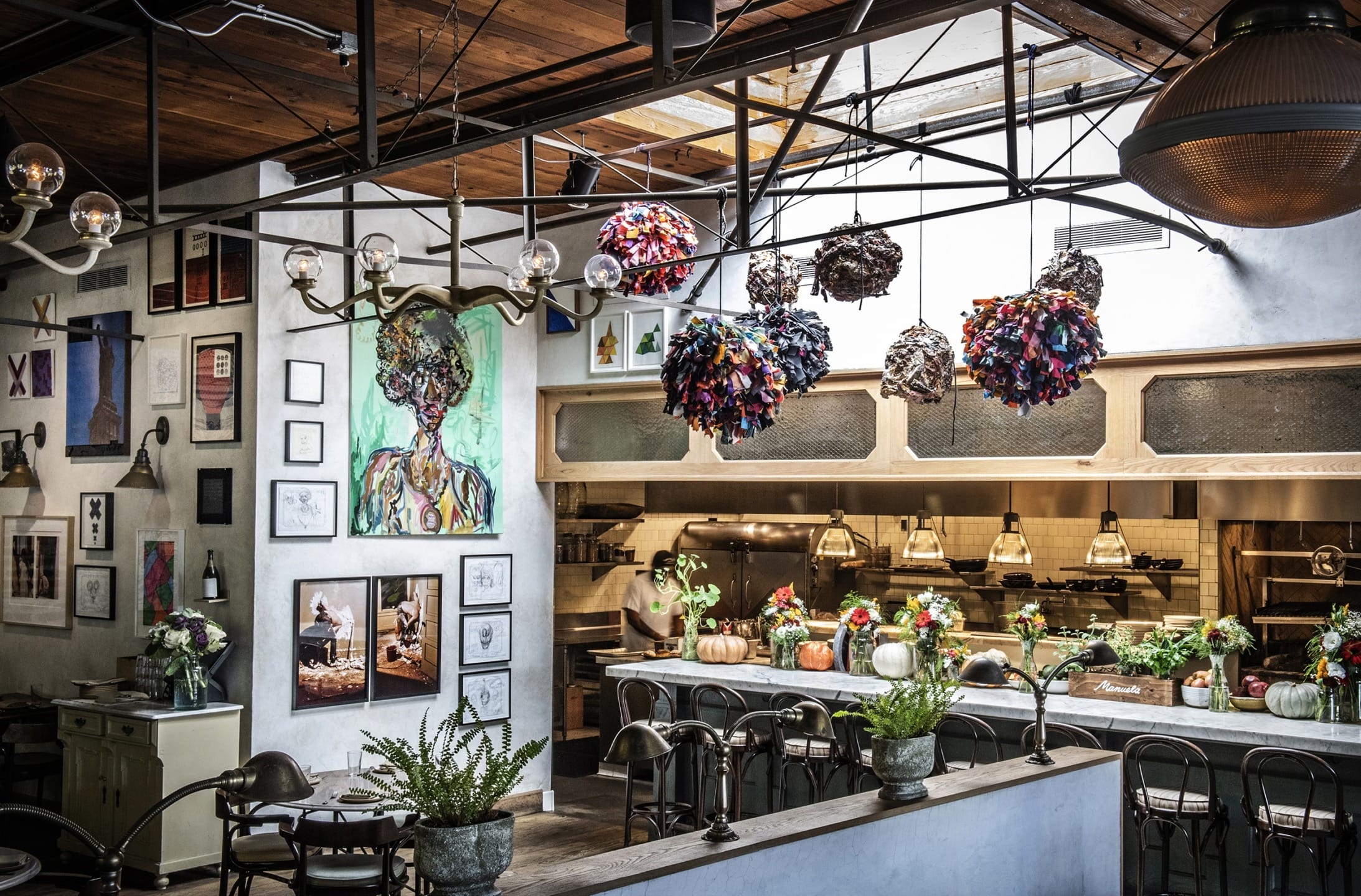 Cozy restaurant interior with art on the walls, eclectic decor, and a mix of greenery and lighting above the dining area.