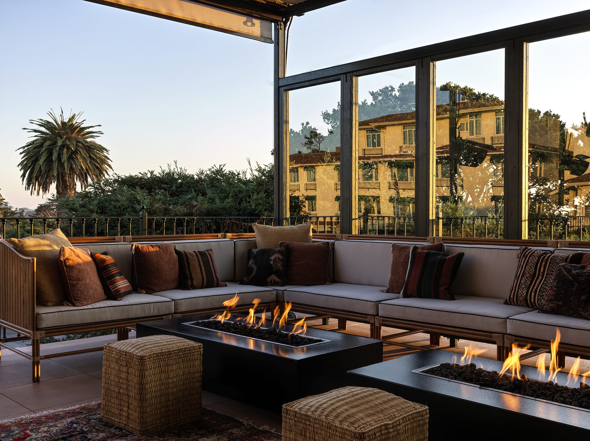 Outdoor patio with modern seating around a lit fire pit, palm tree and buildings visible in the background.