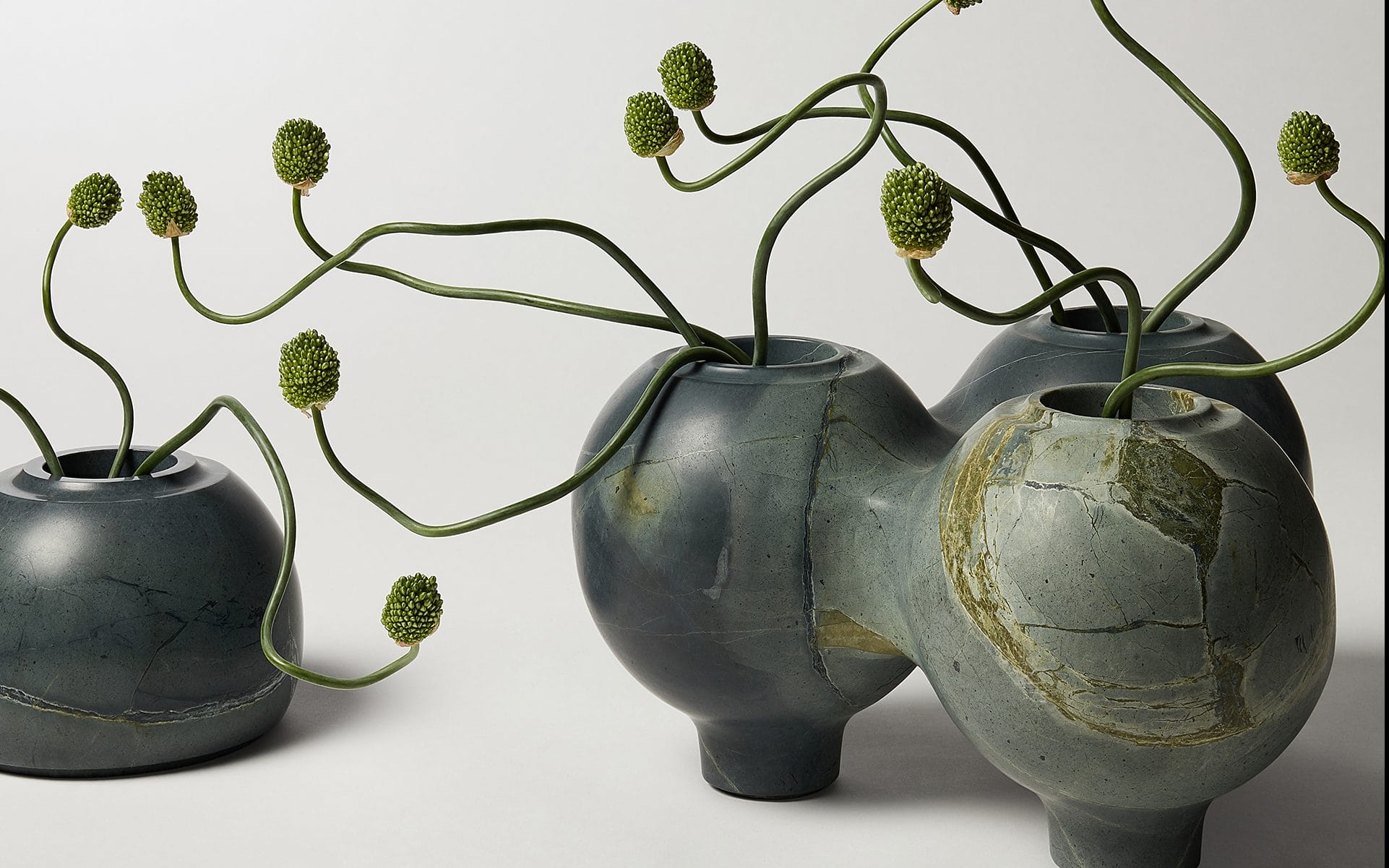 Abstract green vases with curving stems and rounded buds against a plain background.