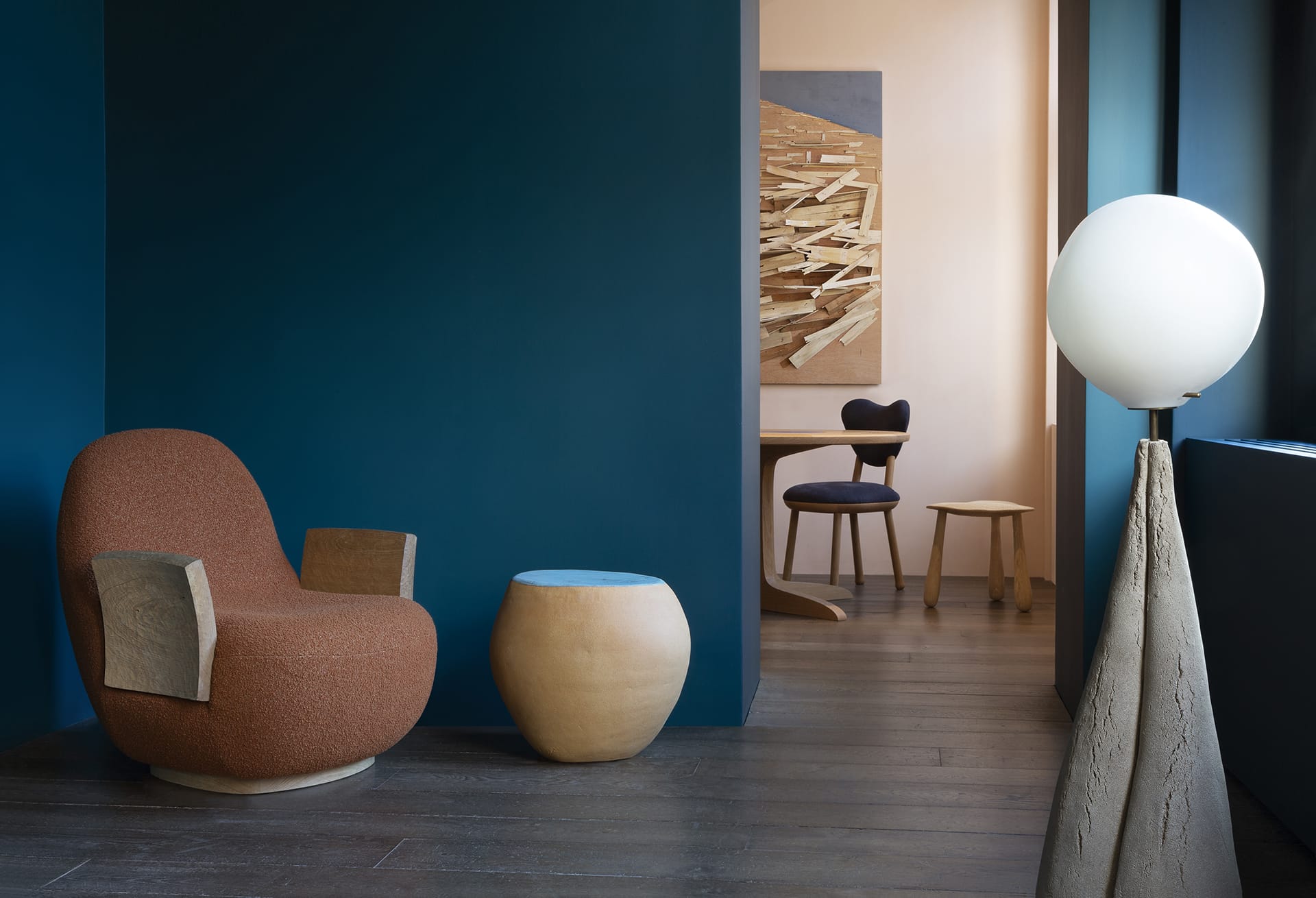 Modern interior with blue walls, a brown chair, light wood stool, abstract artwork, and a stylish floor lamp.