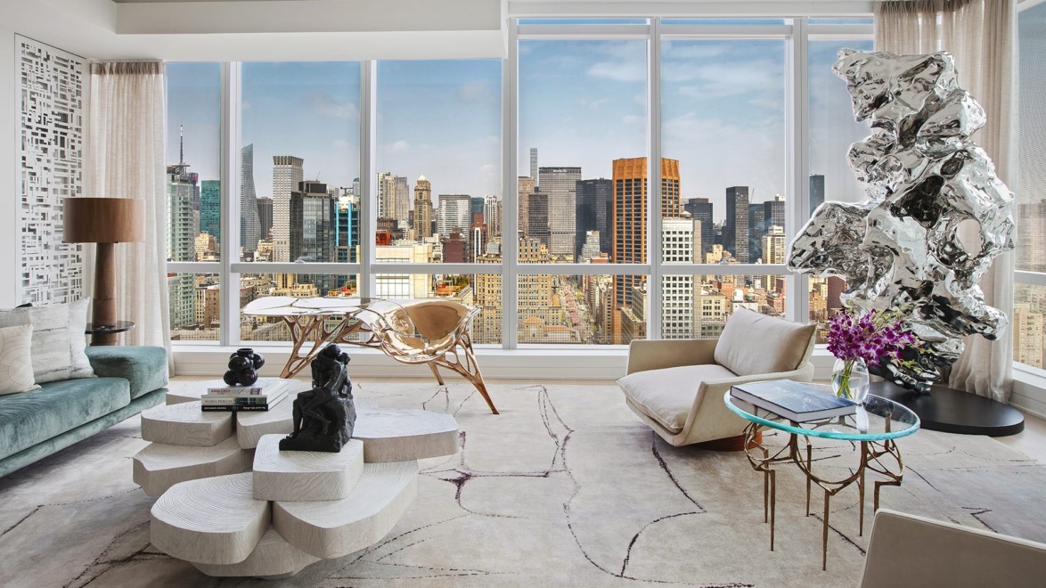 Modern living room with abstract furniture, sculptures, and large windows offering a cityscape view.