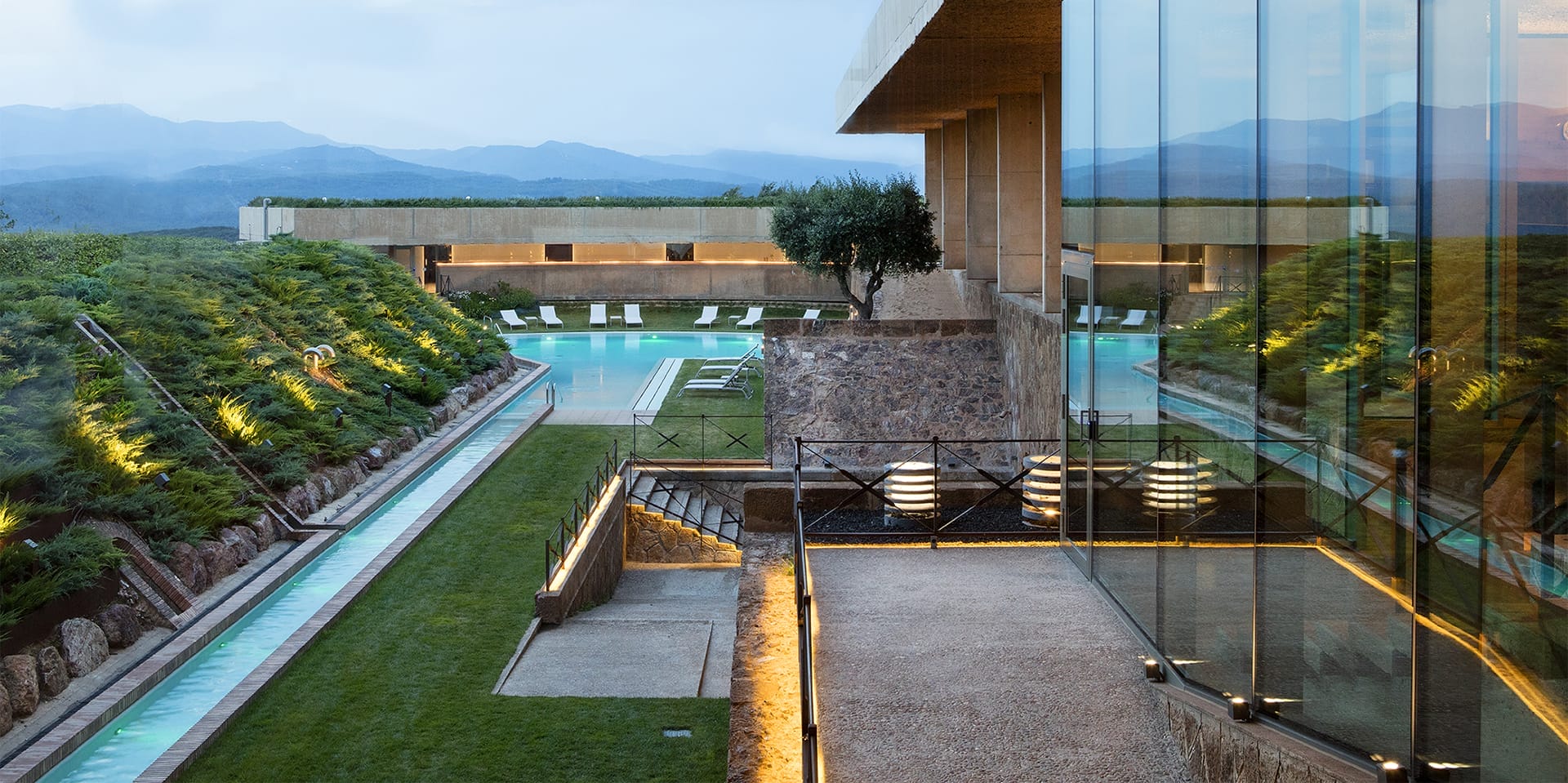Luxury hotel with modern architecture, outdoor pool, lounge chairs, and scenic mountain views at dusk.