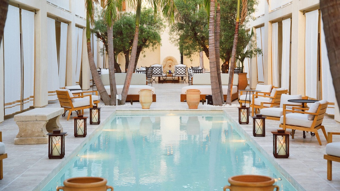 Luxury pool area with palm trees and elegant seating surrounded by lanterns and Mediterranean architecture.