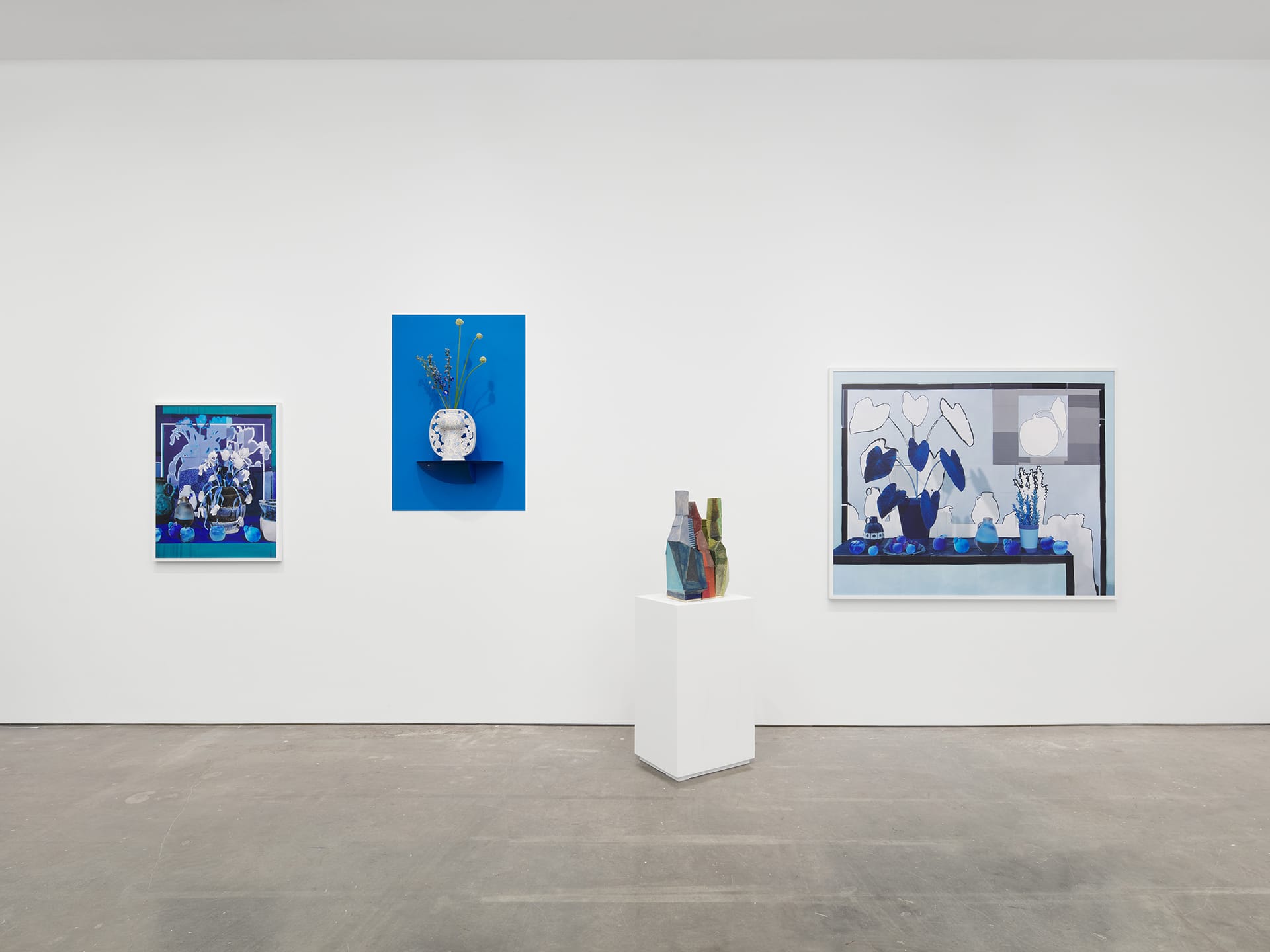 Modern art gallery exhibit featuring blue-themed paintings and pottery displayed against a minimalist white wall.