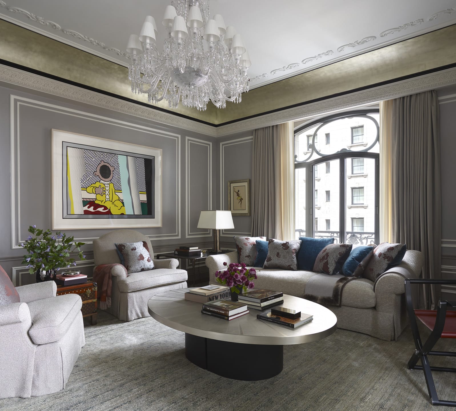 Elegant living room with gray walls, chandelier, pop art painting, and plush seating around a circular coffee table.