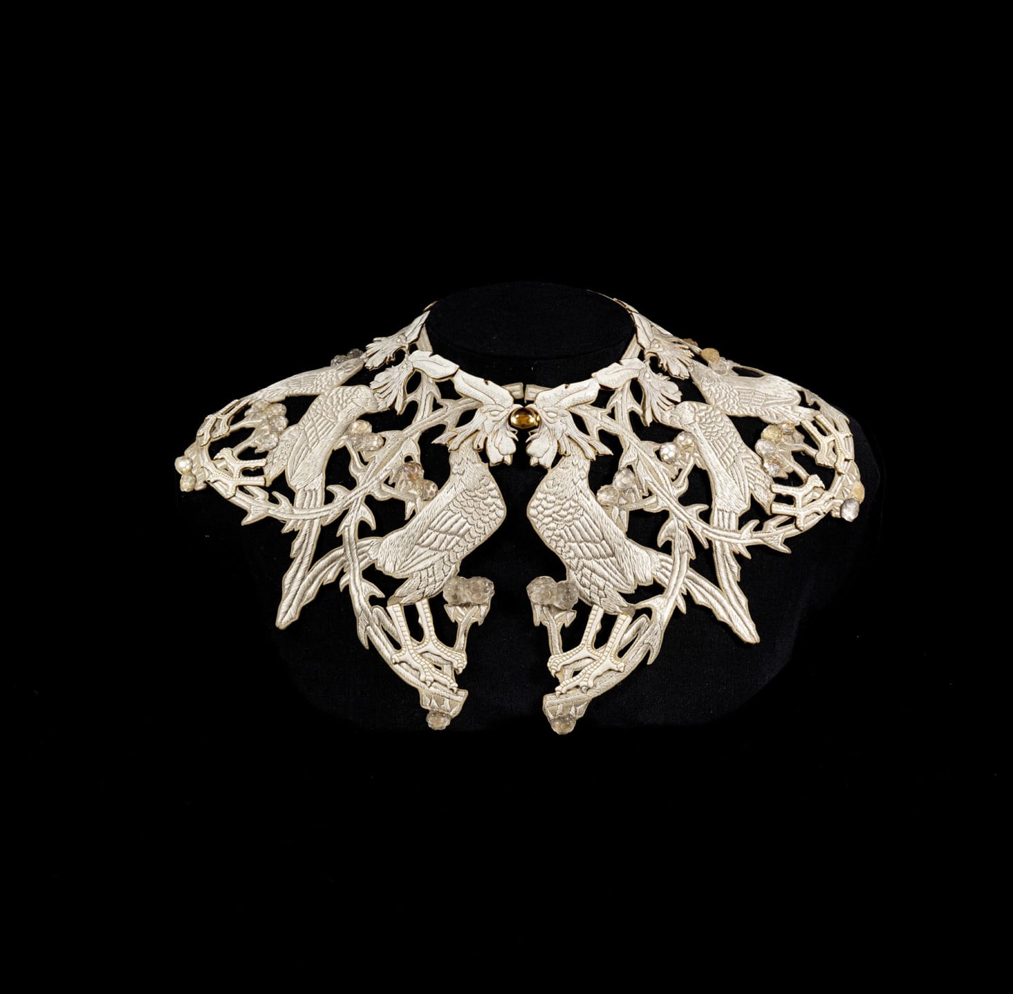Ornate silver necklace featuring intricately carved birds and floral patterns against a black background.