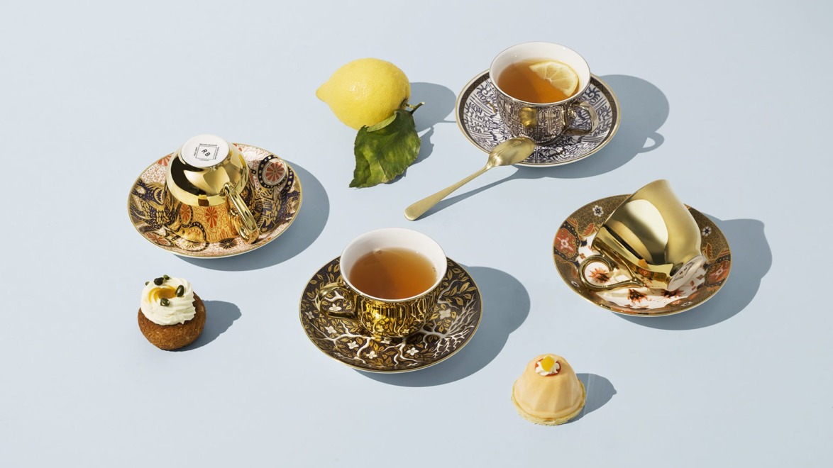 Decorative teacups and saucers with tea, lemon, and small pastries on a light blue background