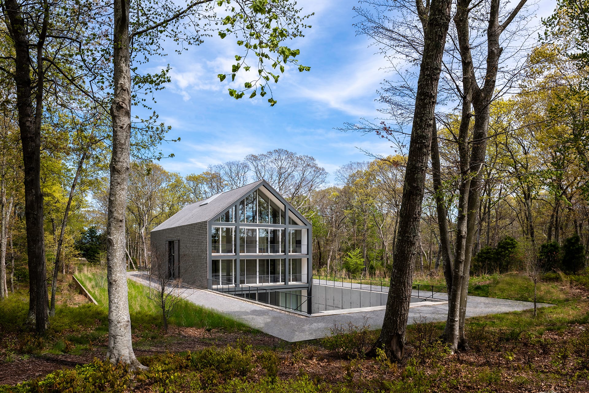 Modern glass and brick house surrounded by trees with a forest backdrop and open skies.