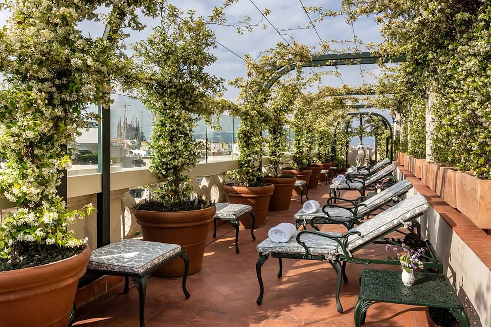 Rooftop terrace with lounge chairs and lush greenery under a blue sky.