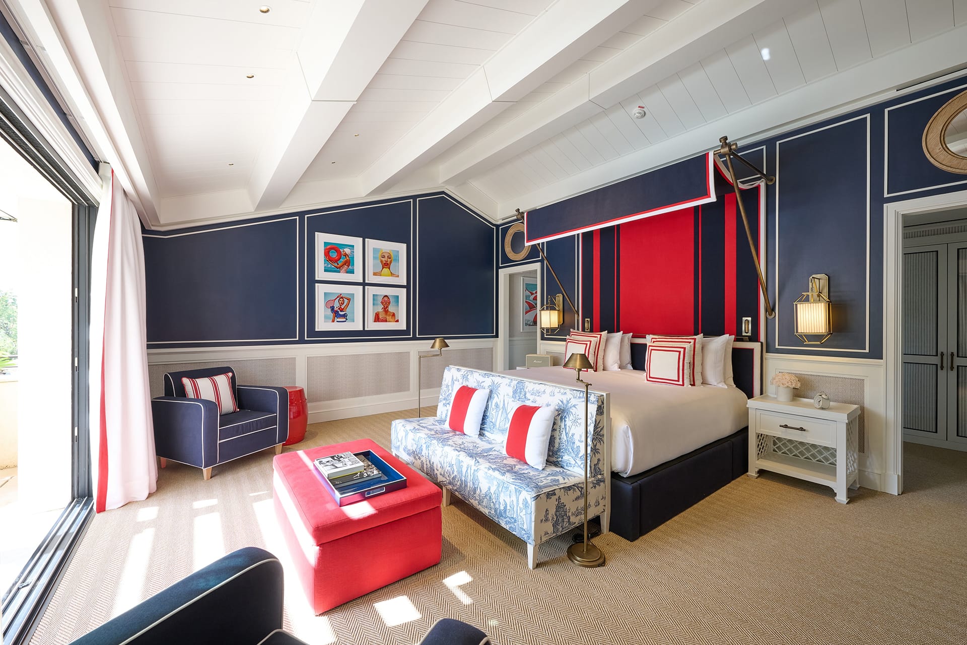 Luxurious hotel room with nautical-themed decor, featuring a king-size bed, navy and red colors, and stylish furniture.