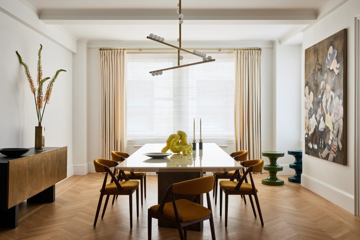 Modern dining room with a sleek table, mustard chairs, contemporary chandelier, and abstract artwork on the wall.