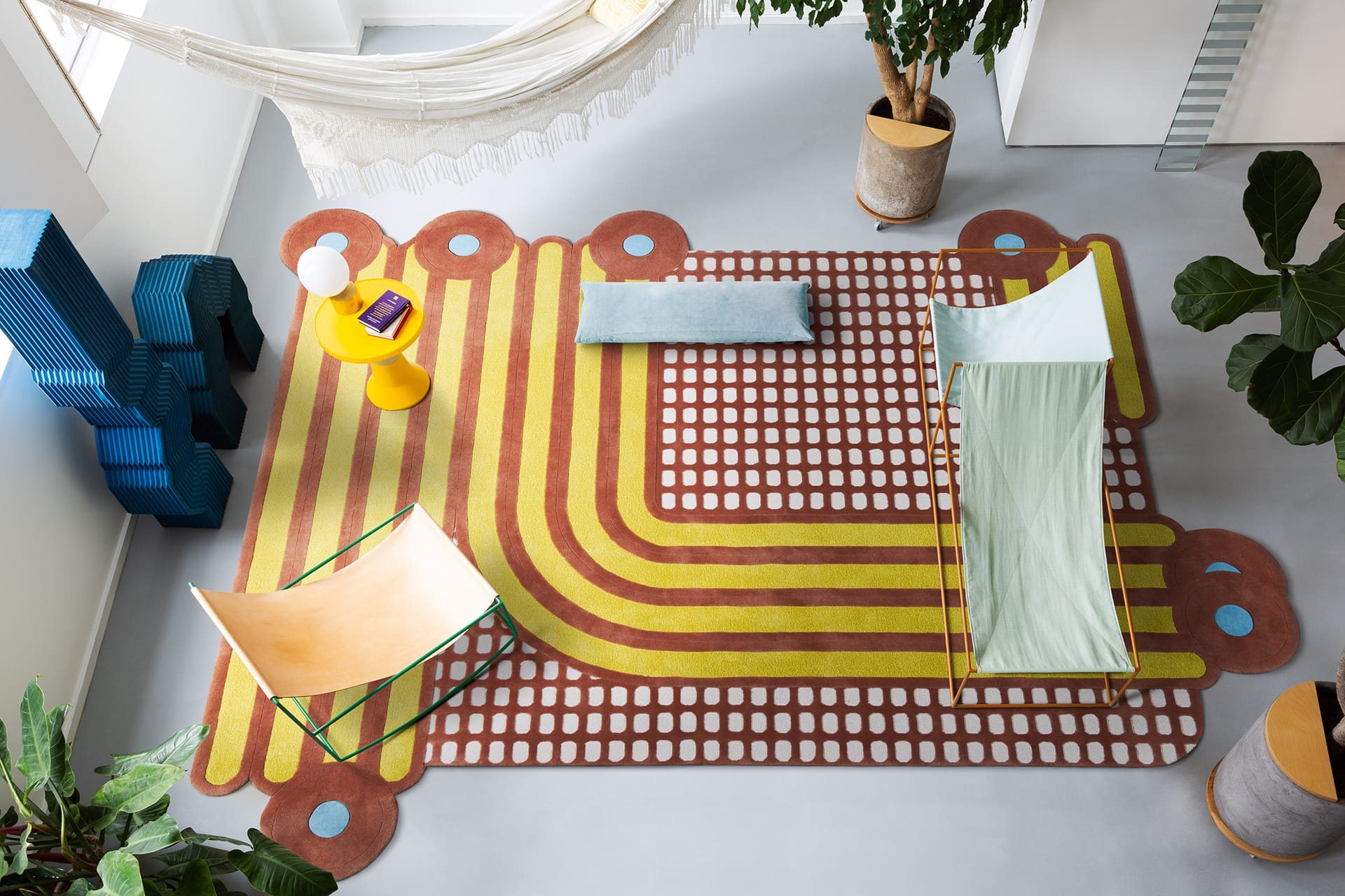 Modern living space with a colorful rug, hammock, plants, and contemporary furniture viewed from above.