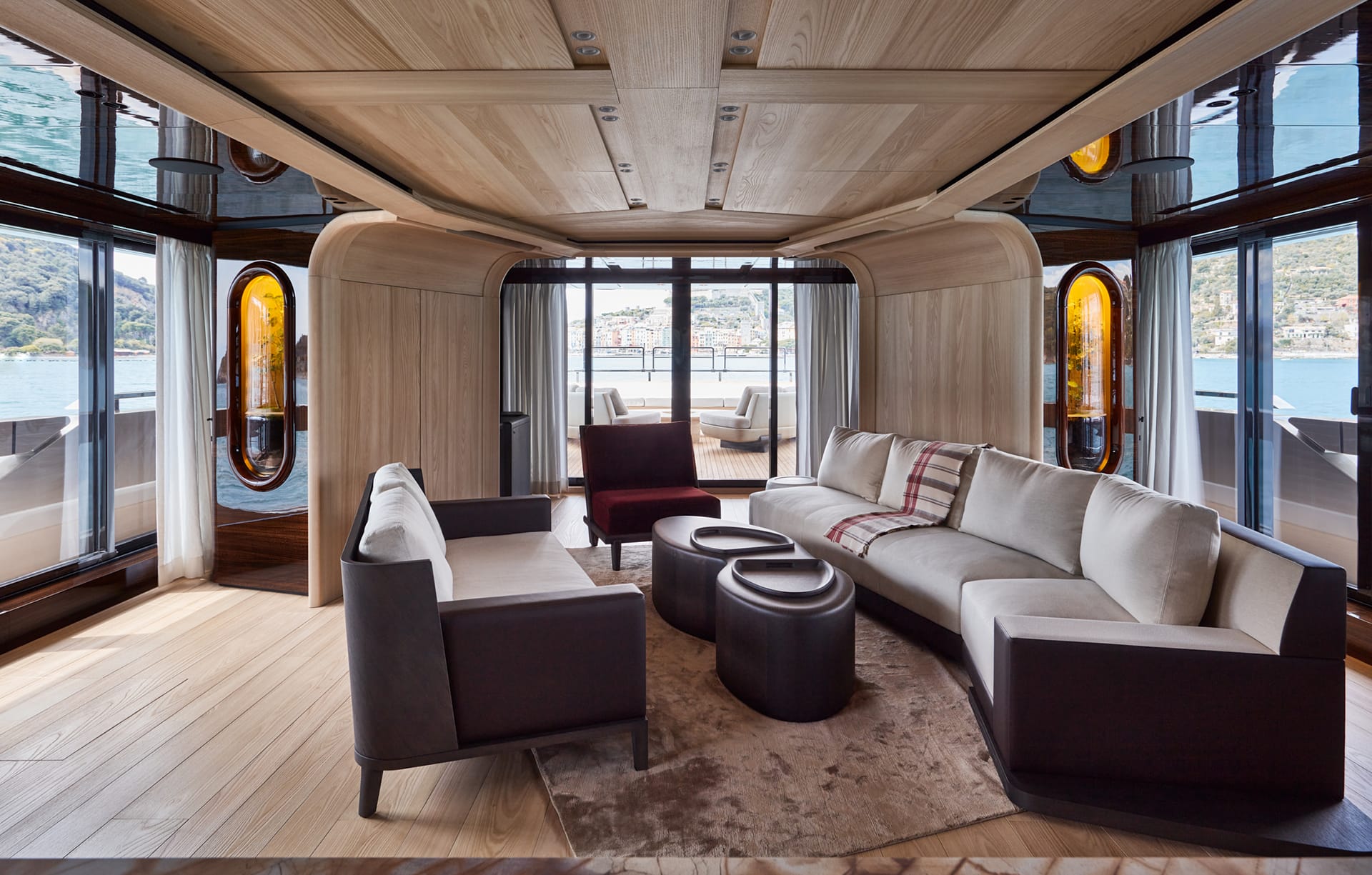 Luxurious yacht interior with modern furniture, wood paneling, and large windows overlooking a scenic view of water and mountains.