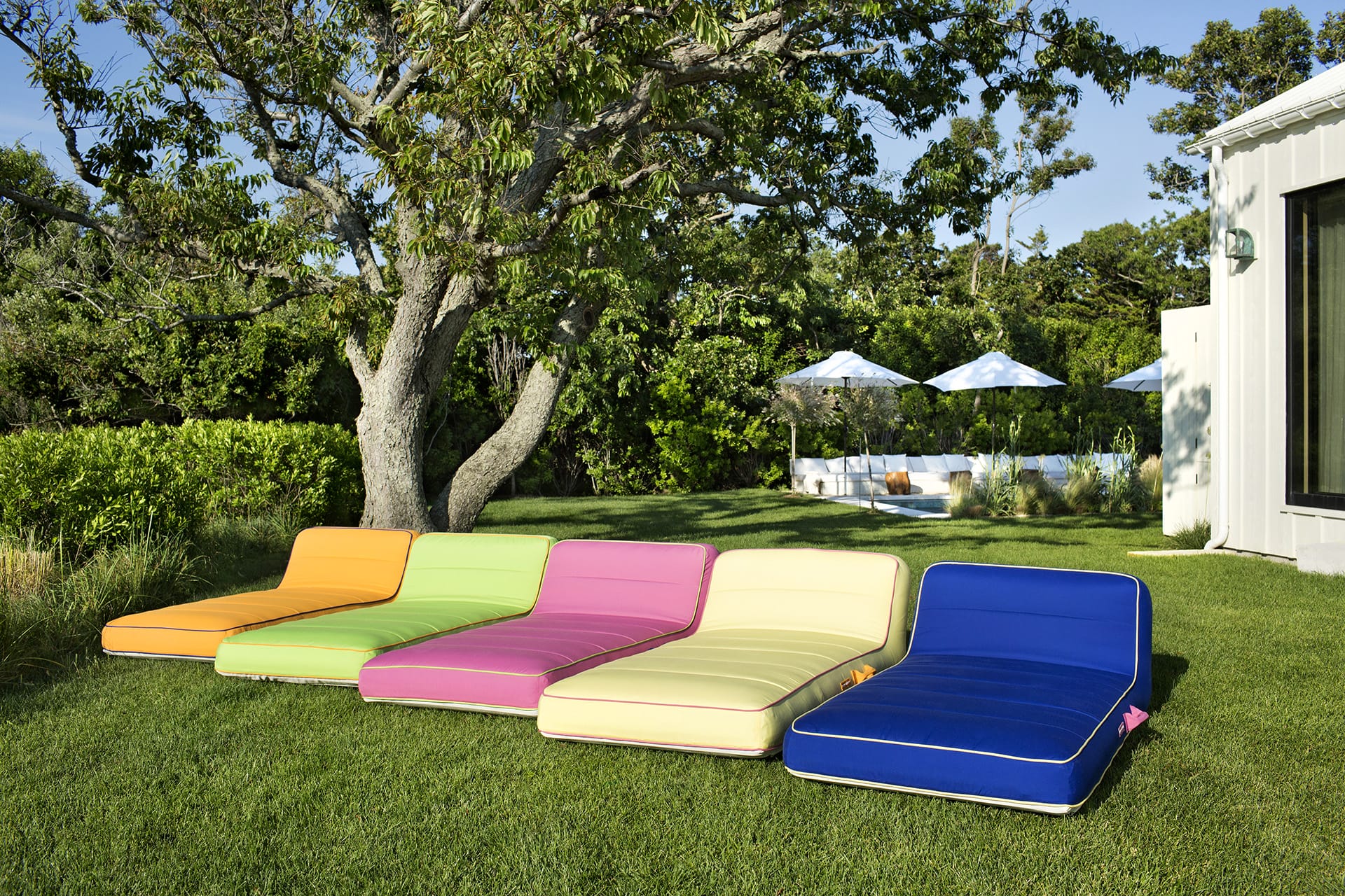 Colorful outdoor lounge chairs on grass with trees and umbrellas in the background on a sunny day.