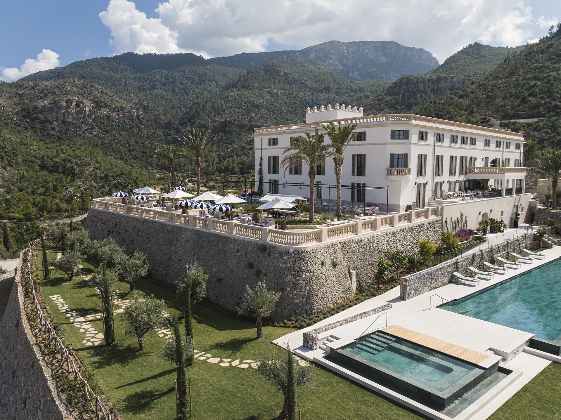 Historic luxury hillside hotel with outdoor pool and terrace overlooking lush green mountains and clear blue sky.