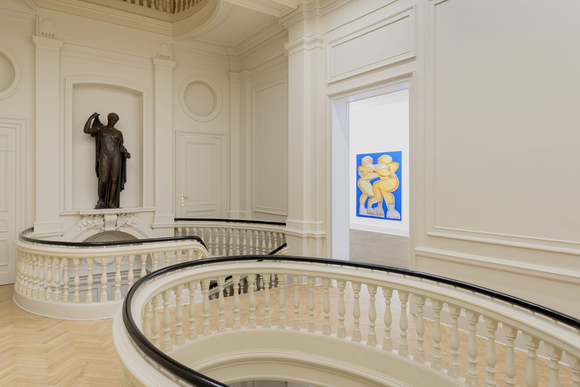 Elegant interior with curved staircase, classical statue, and a modern colorful artwork in a brightly lit gallery space.