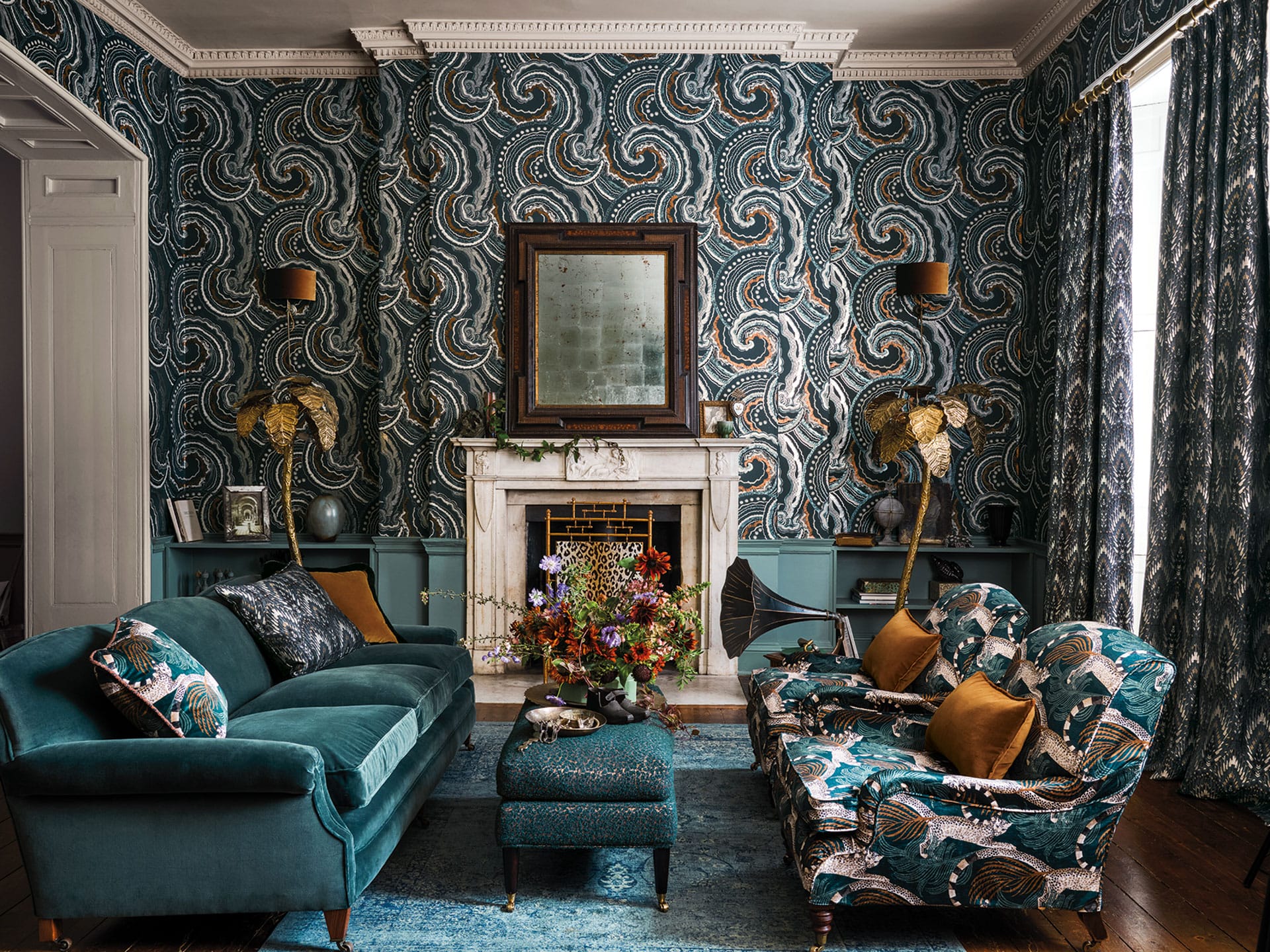 Luxurious living room with ornate wallpaper, velvet sofa, patterned armchairs, and an ornate fireplace with floral arrangement.