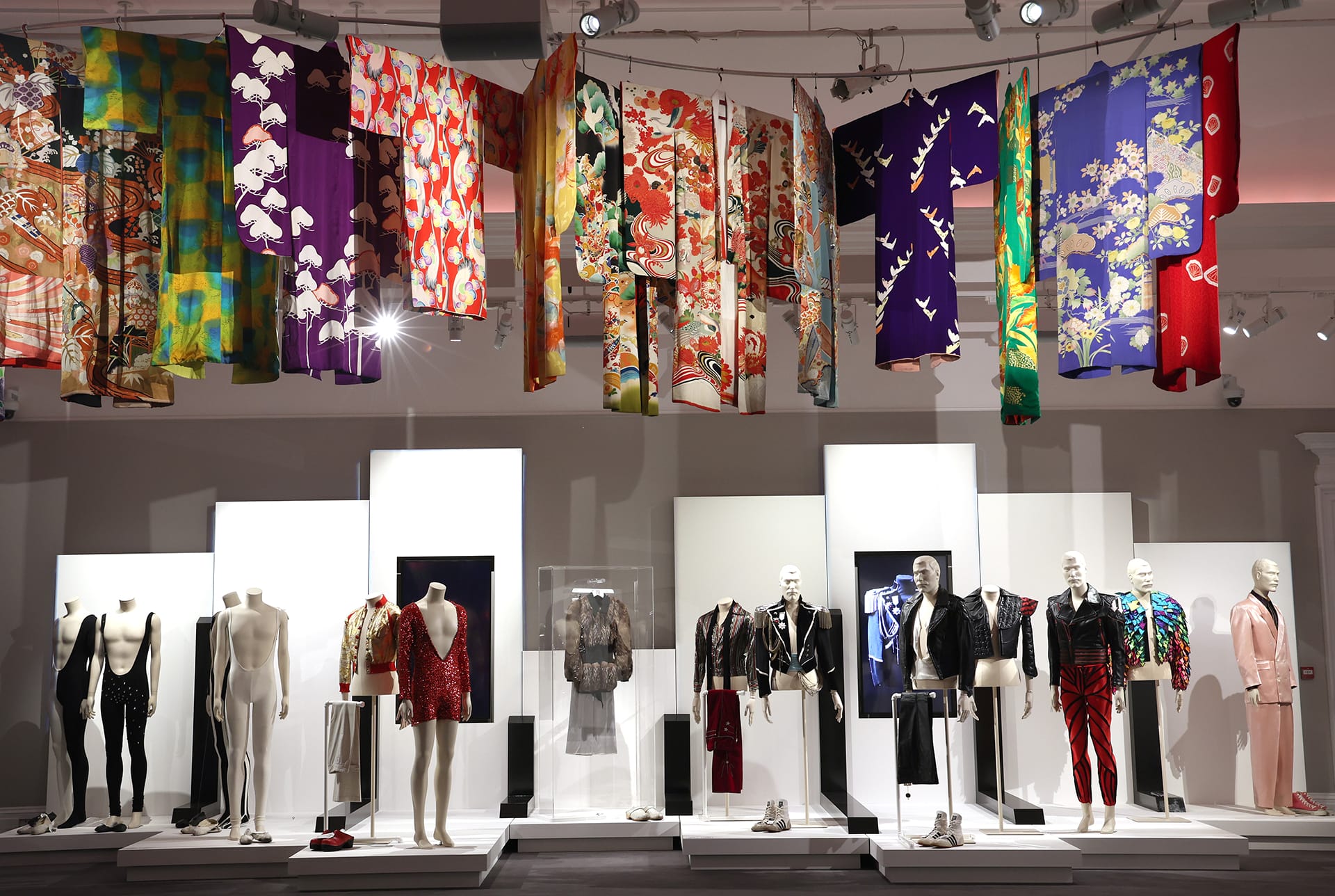 Exhibit showcasing vibrant kimonos and mannequins in eclectic designer outfits on display in a well-lit gallery setting.