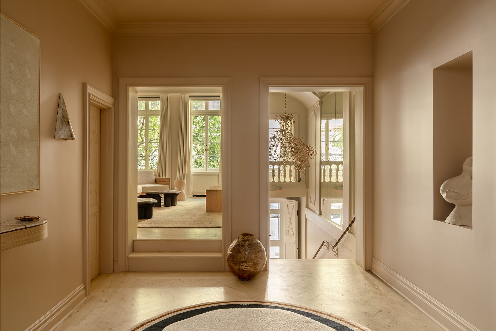 Elegant home interior with warm beige tones, large windows, and minimalistic decor, featuring a round rug and a ceramic vase.