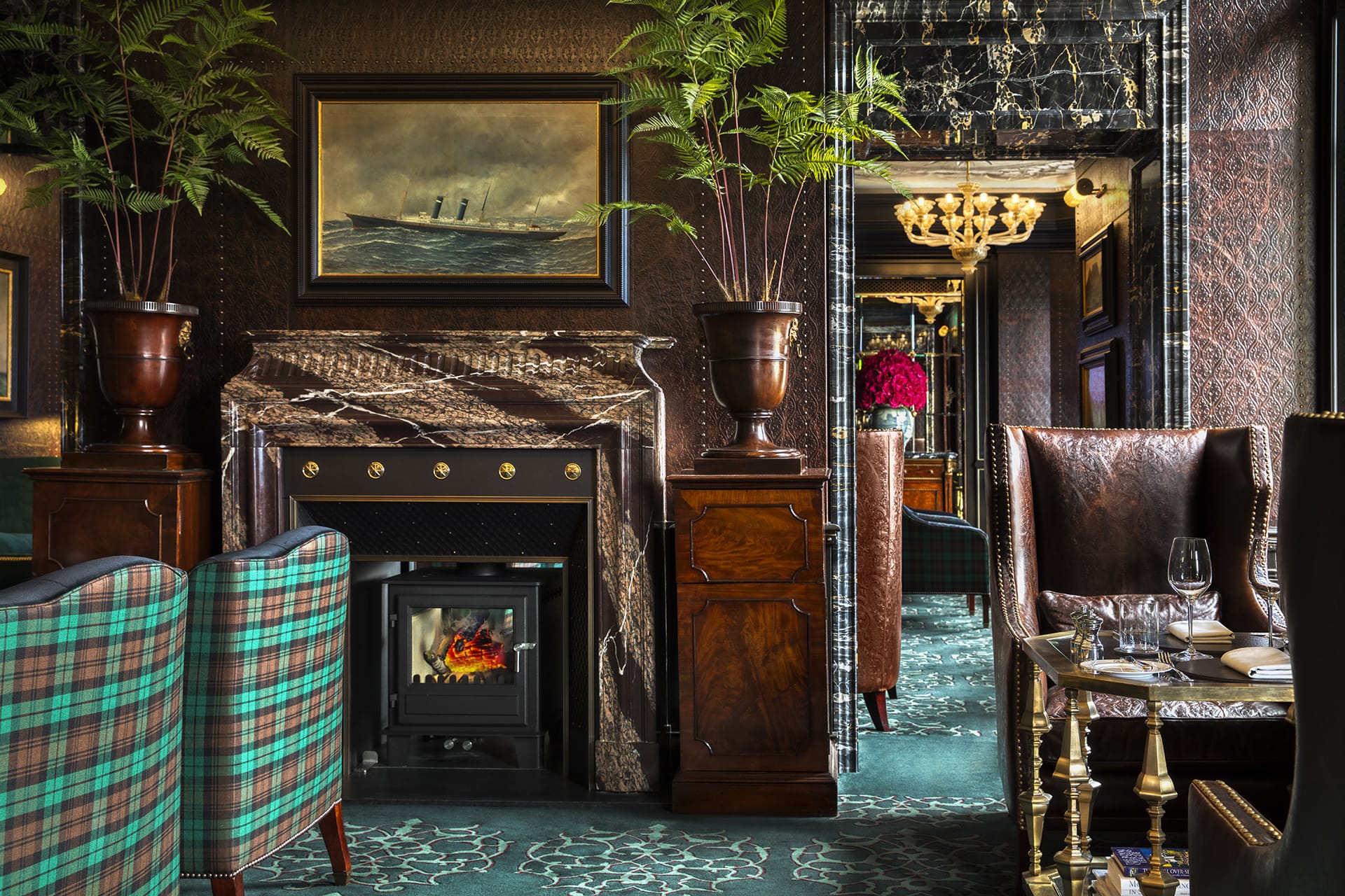 Luxurious living room with green plaid chairs, ornate fireplace, ship painting, and elegant decor.