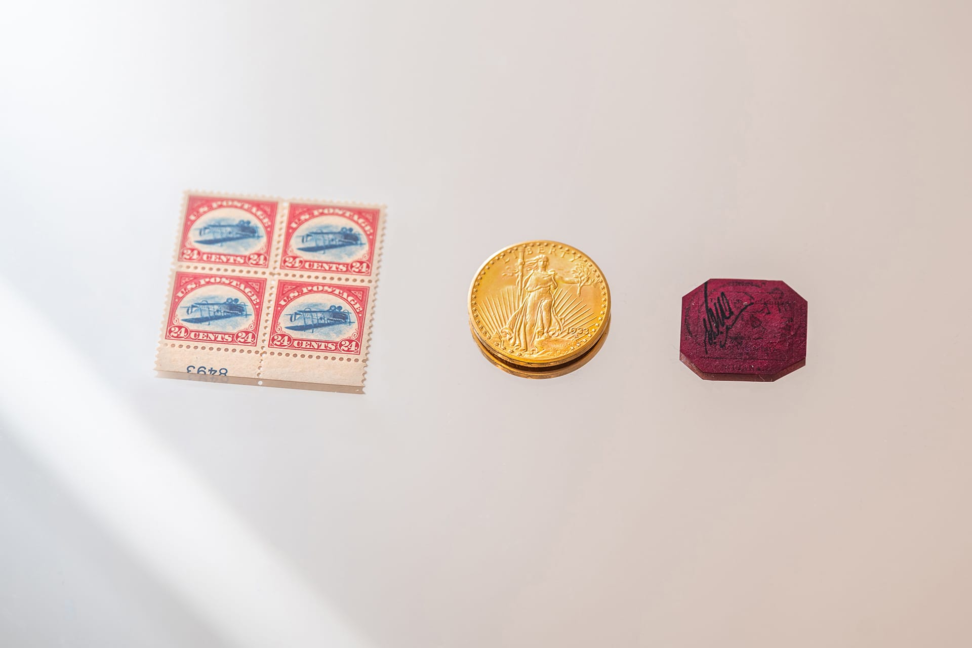 Uncut sheet of vintage stamps, a gold coin, and a unique red stamp displayed on a reflective surface.