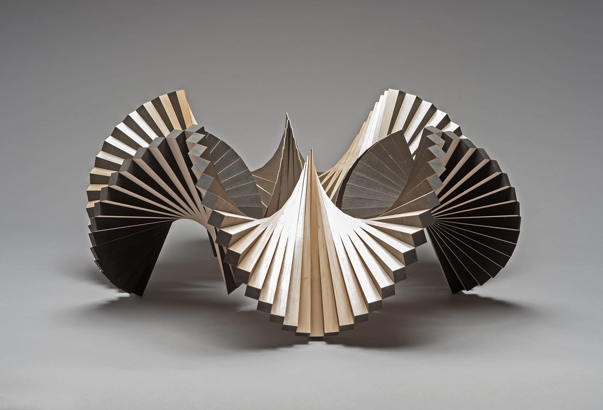Abstract geometric sculpture with folded wooden panels creating a dynamic and intricate design on a neutral background