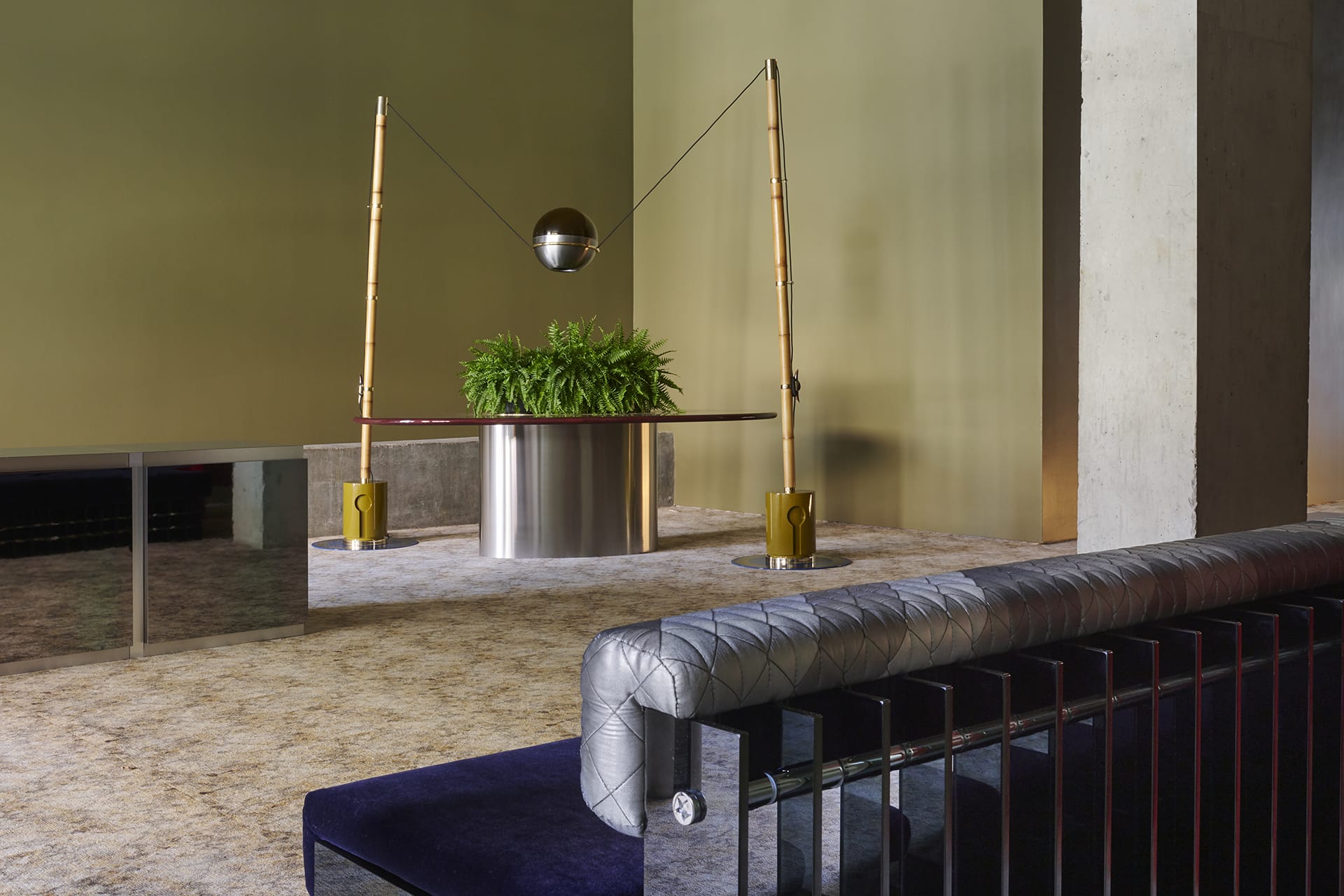 Modern lobby interior with a stylish bench, metallic planter with greenery, and unique lighting fixture.