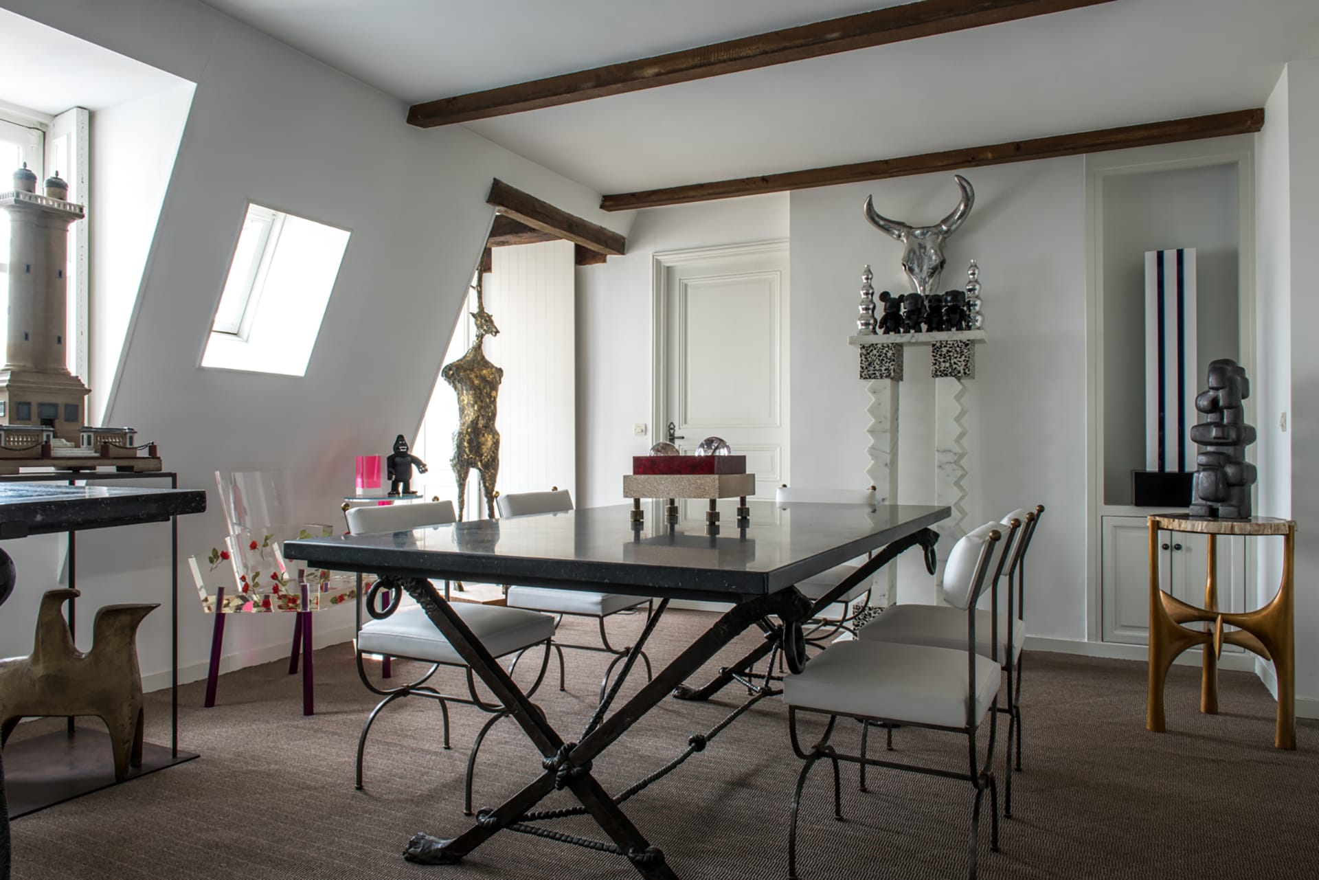 Eclectic dining room with mix of modern and antique sculptures, metal table, unique decor, and slanted windows.