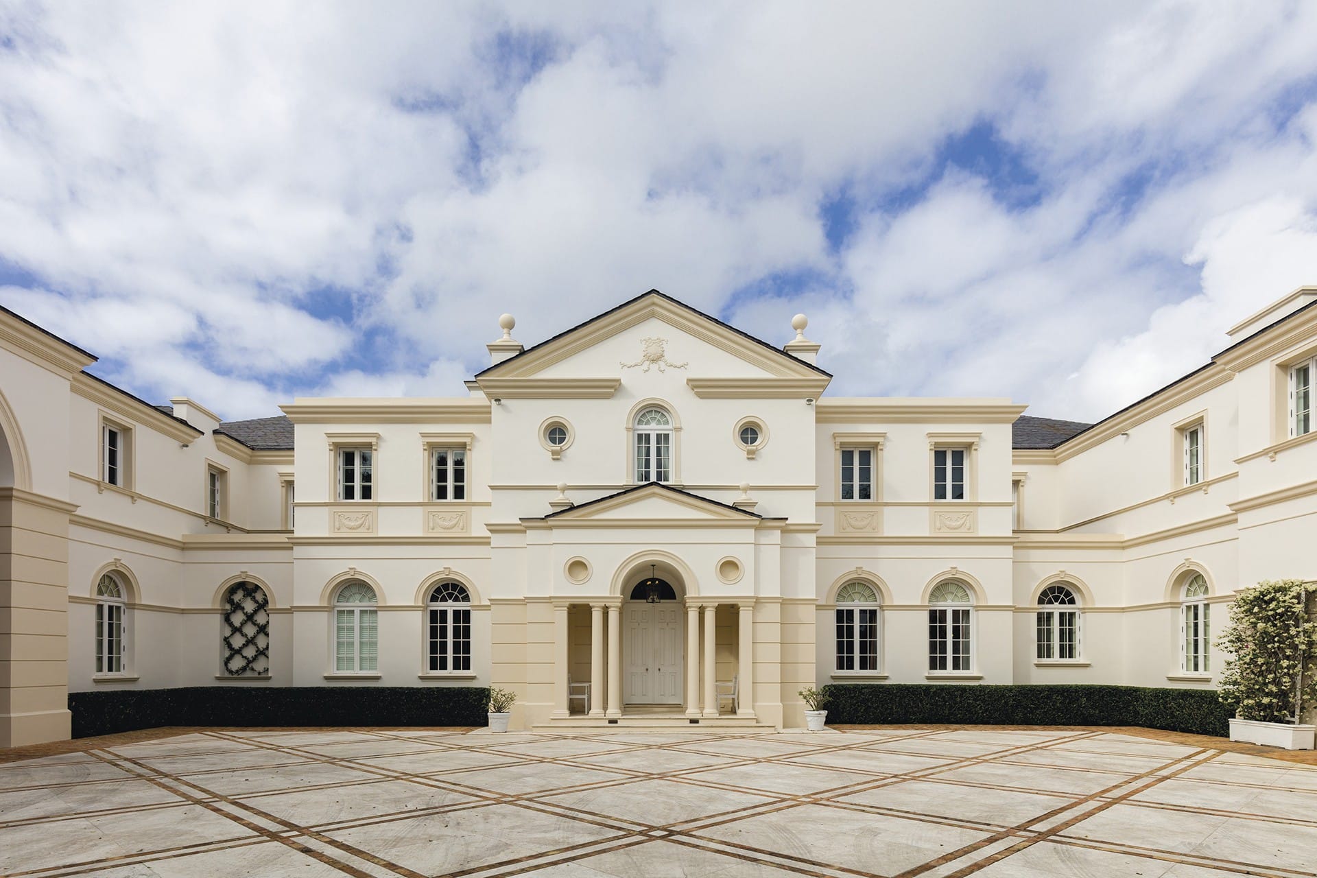 Elegant mansion with symmetrical architecture, arched windows, and grand entrance against a partly cloudy sky.