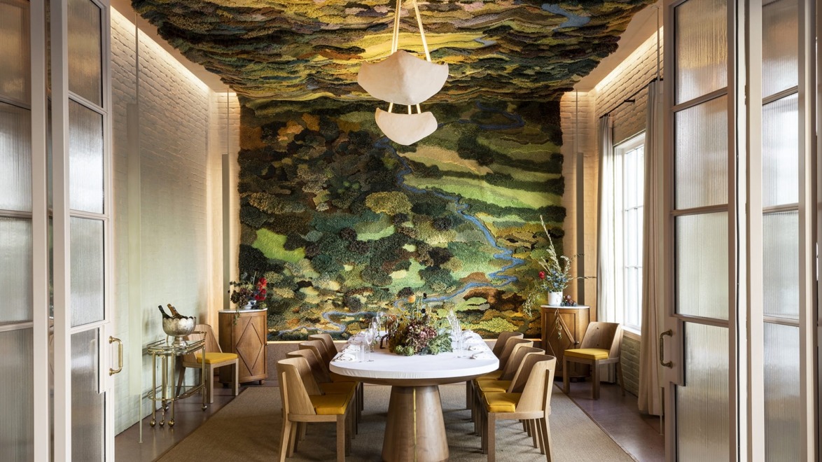 Elegant dining room with a large round table, surrounded by chairs, and a vibrant nature-themed wall and ceiling design.