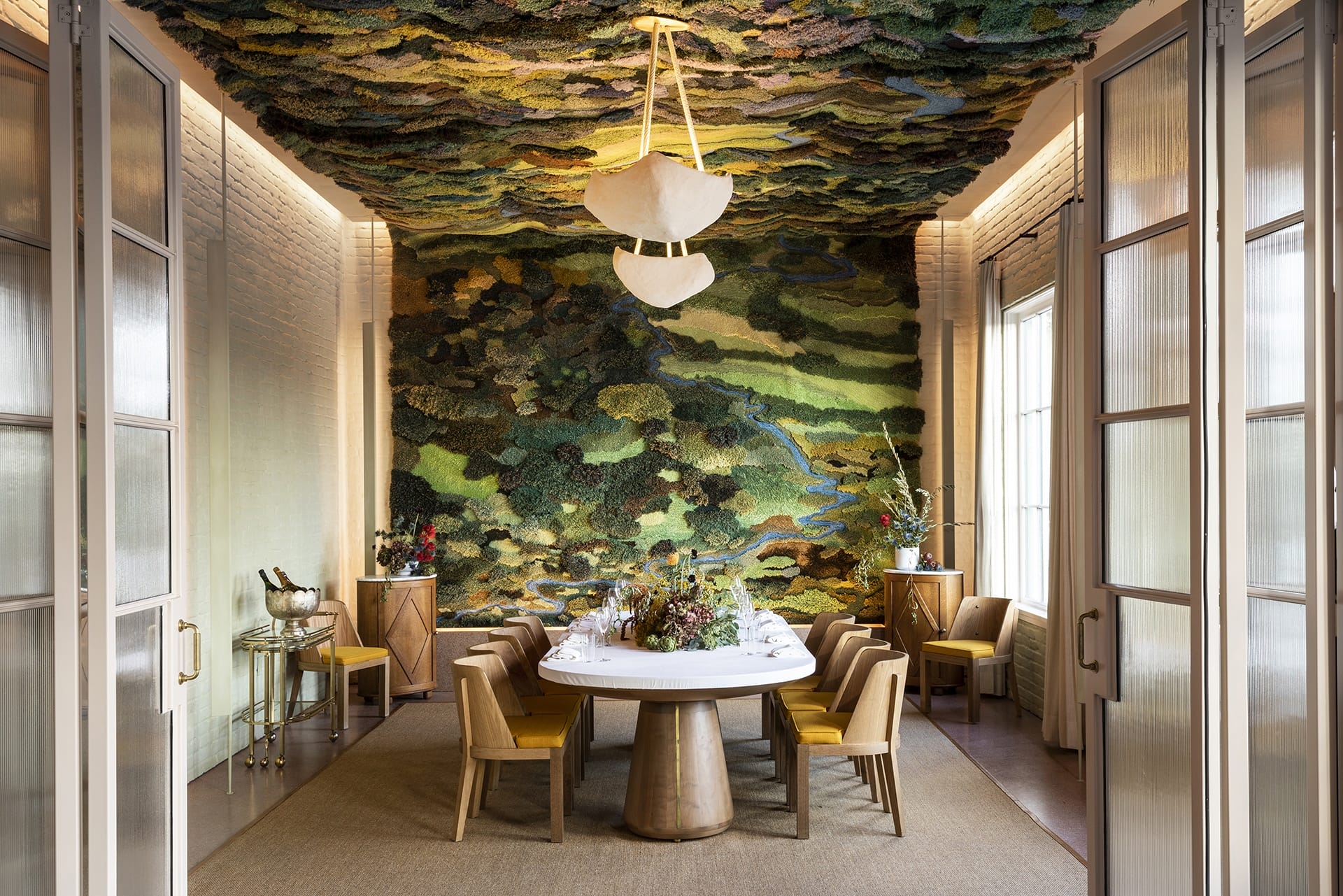 Elegant dining room with a large round table, surrounded by chairs, and a vibrant nature-themed wall and ceiling design.