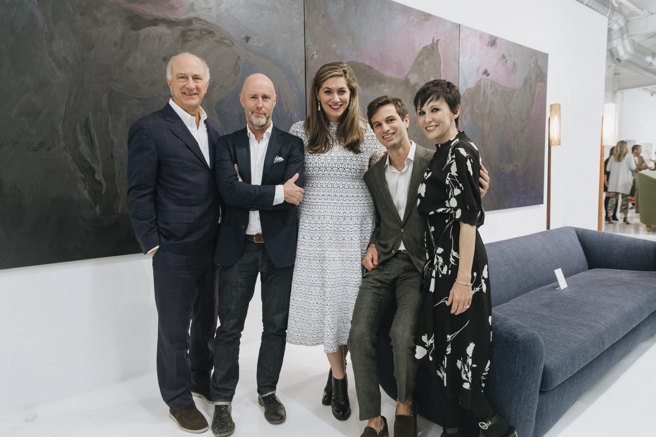 Group of five people smiling and posing in front of a large abstract painting at an art gallery.