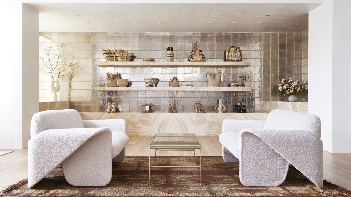 Modern living room with white sofas, elegant coffee table, decorative shelves, and a metallic tiled back wall.