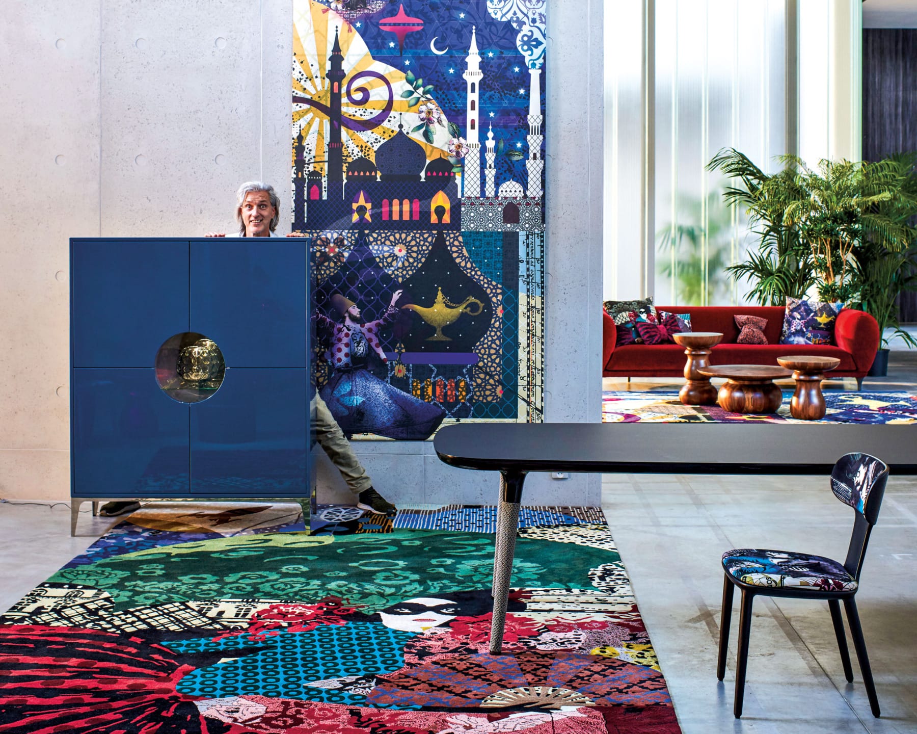 Colorful, eclectic living room with patterned carpet, unique art, modern furniture, and lush plants in bright, airy space.