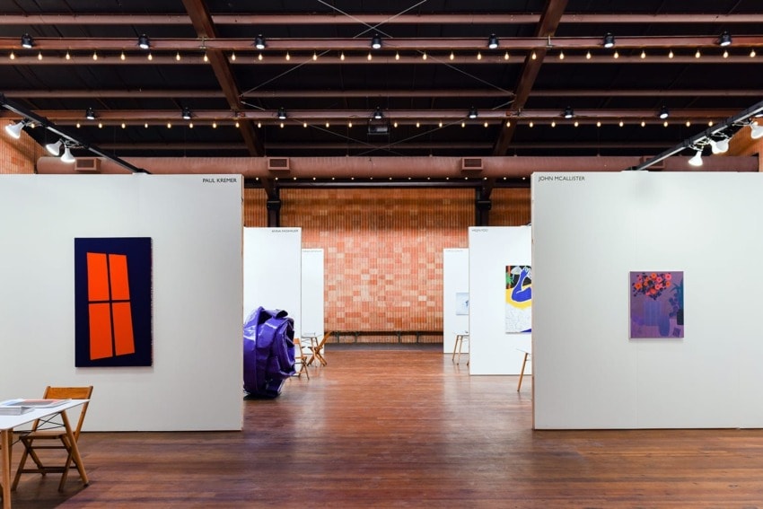 Art gallery interior with various colorful abstract paintings displayed on white walls and wooden floor.